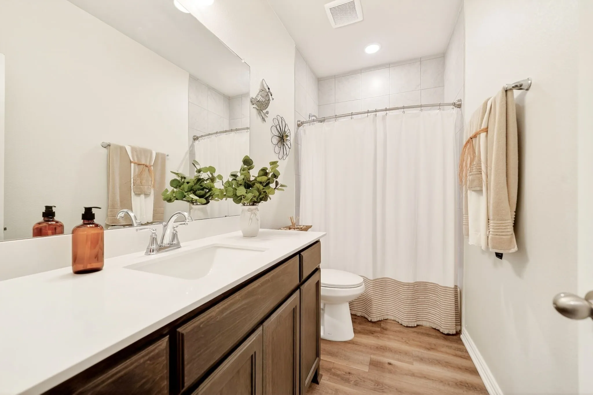 Bathroom featuring a wood-finish vanity with a white countertop and integrated sink, a large wall-mounted mirror, and a shower with tiled walls