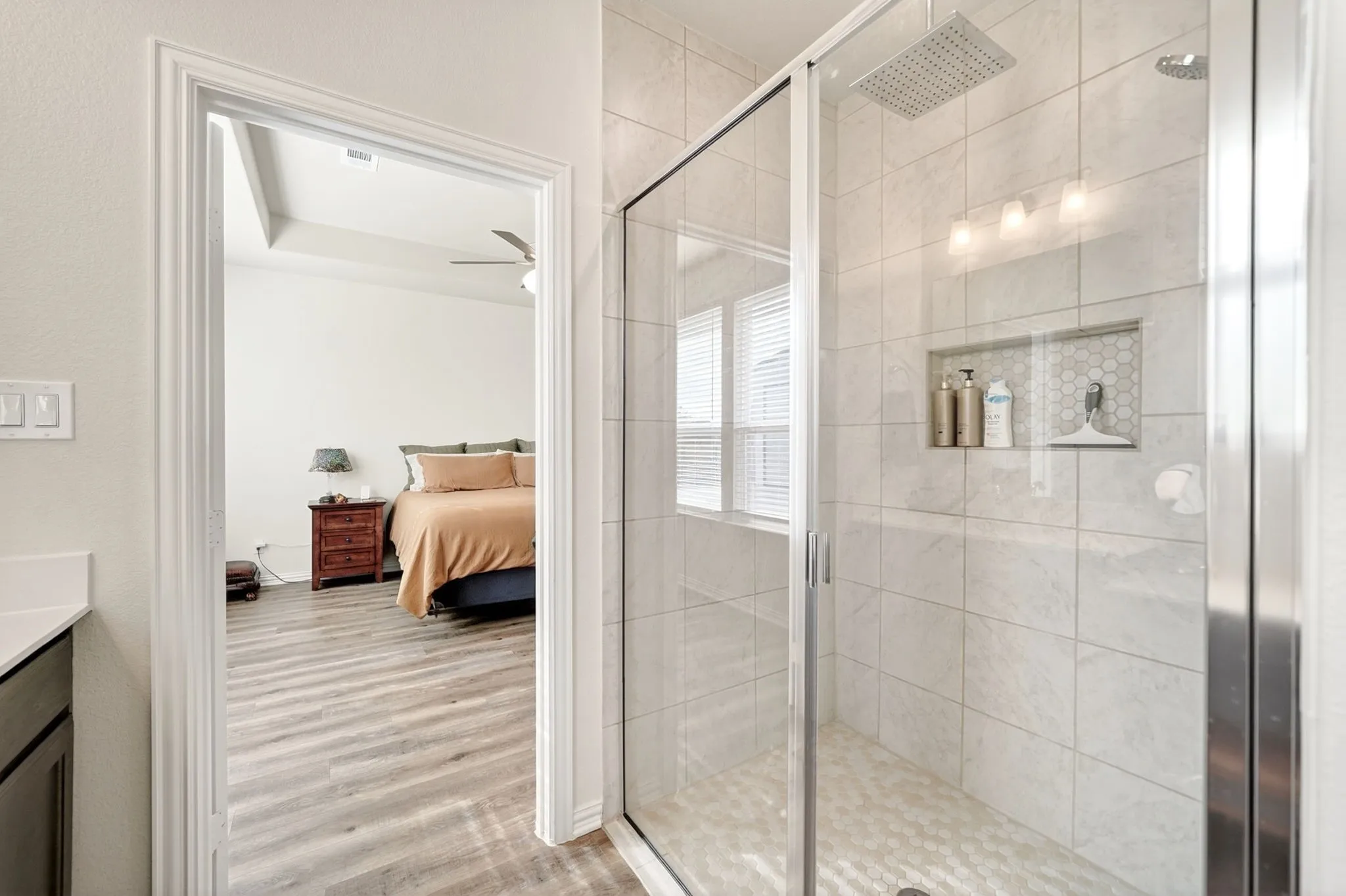 Glass-enclosed shower with a rain showerhead, light-toned tile surround, recessed tile niche, and hexagonal tile shower floor