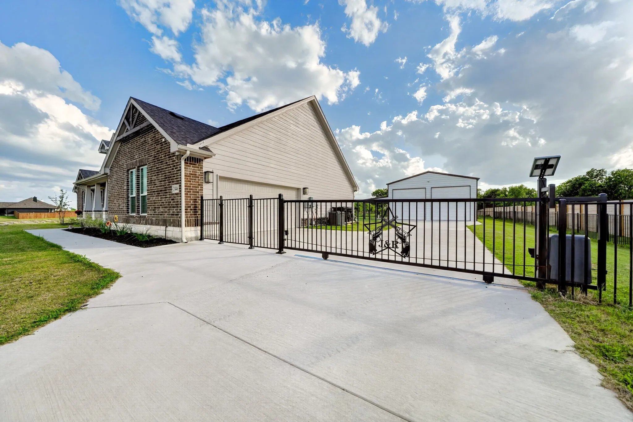 Newly constructed home featuring a stone and siding exterior with a welcoming front facade, complemented by an expansive concrete driveway and professional black metal fencing
