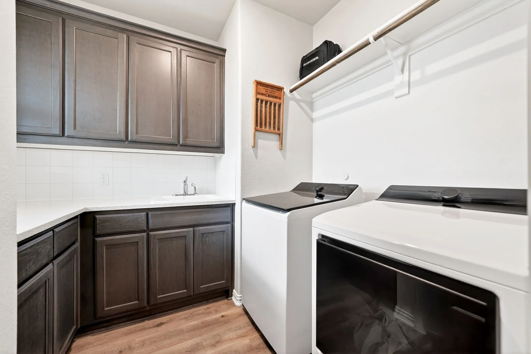 Dedicated laundry space featuring extensive cabinetry, white countertops, a utility sink with faucet, white tile backsplash, and wood-finish flooring