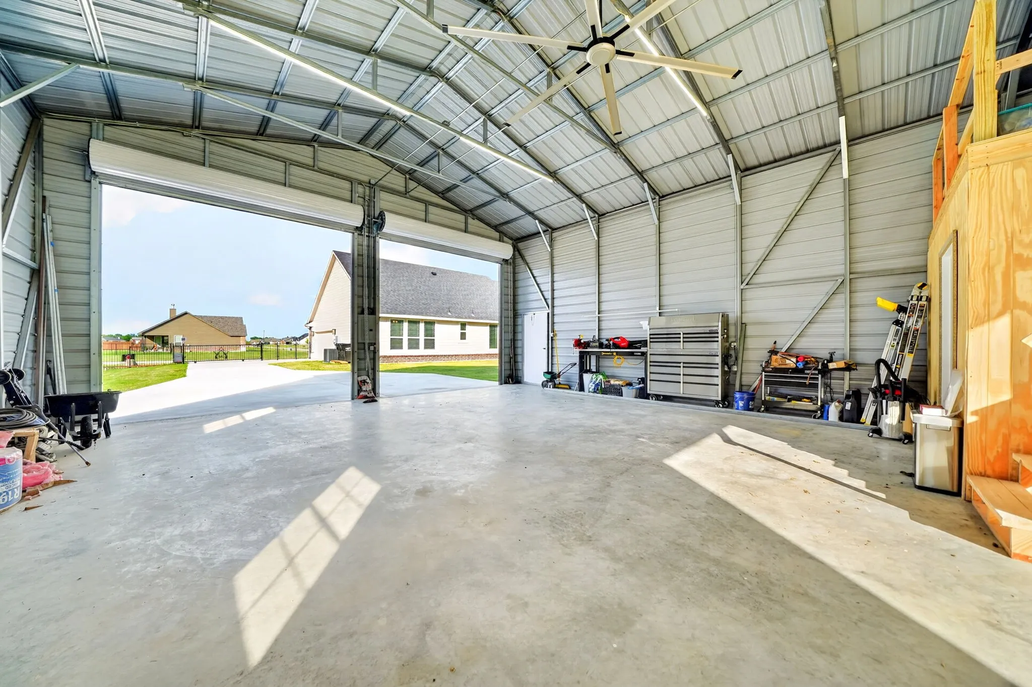 Spacious metal outbuilding featuring high ceilings, two large roll-up doors, a finished concrete floor, and a built-in wood-frame loft