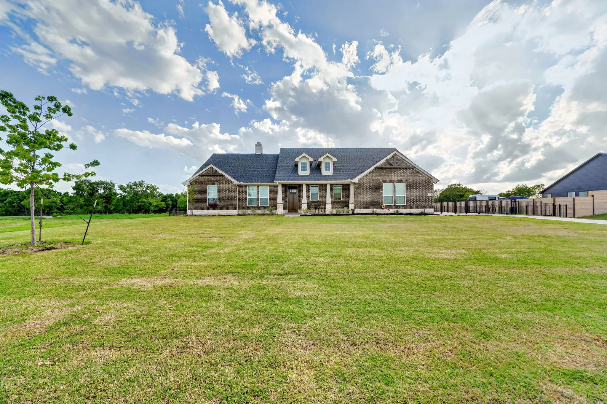 Expansive front lawn with a single-story home featuring a brick facade, dark shingle roof, and multiple windows