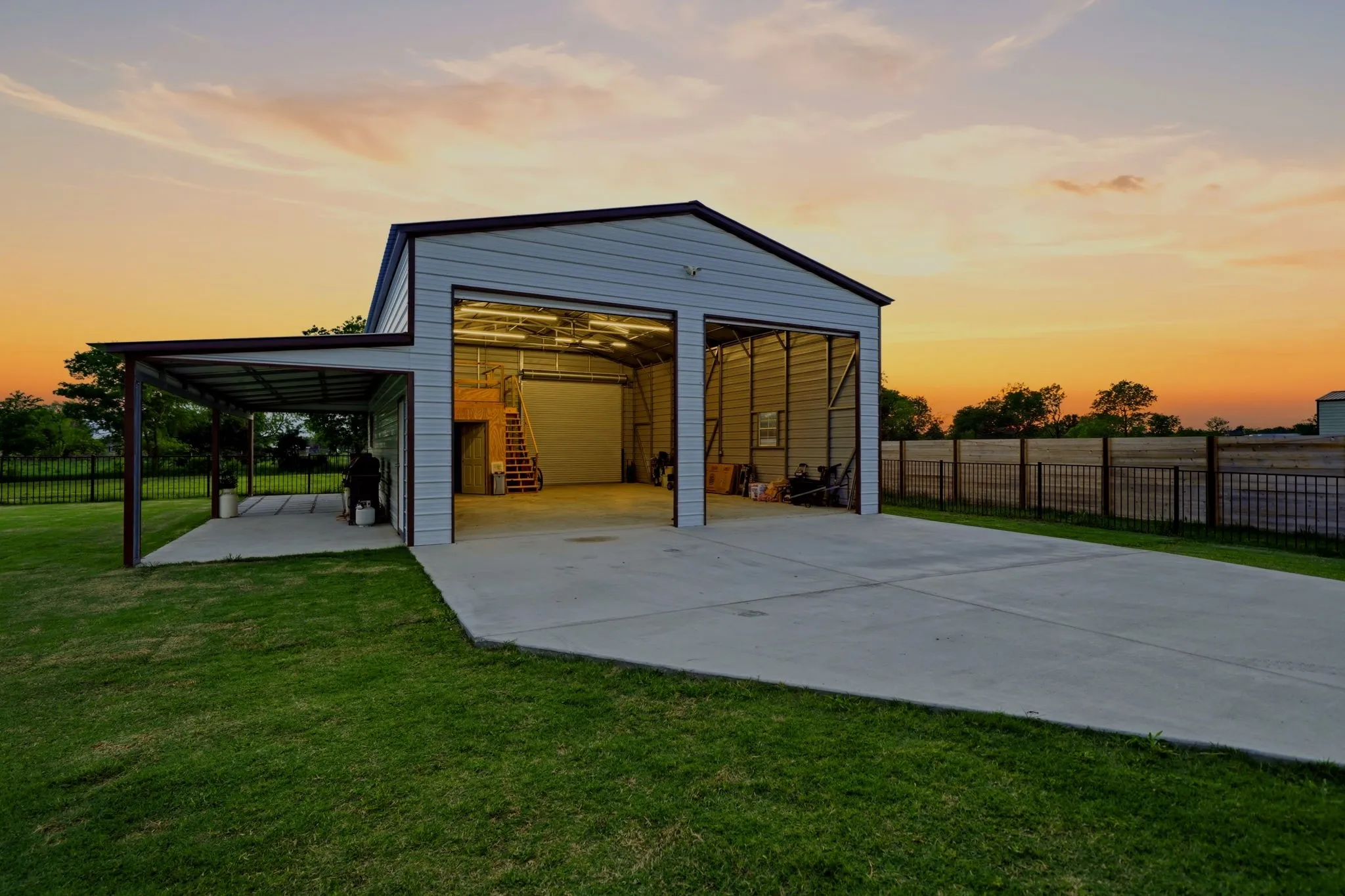 Metal-sided multi-bay garage with concrete slab foundation, multiple overhead doors, interior staircase, and an attached covered concrete patio