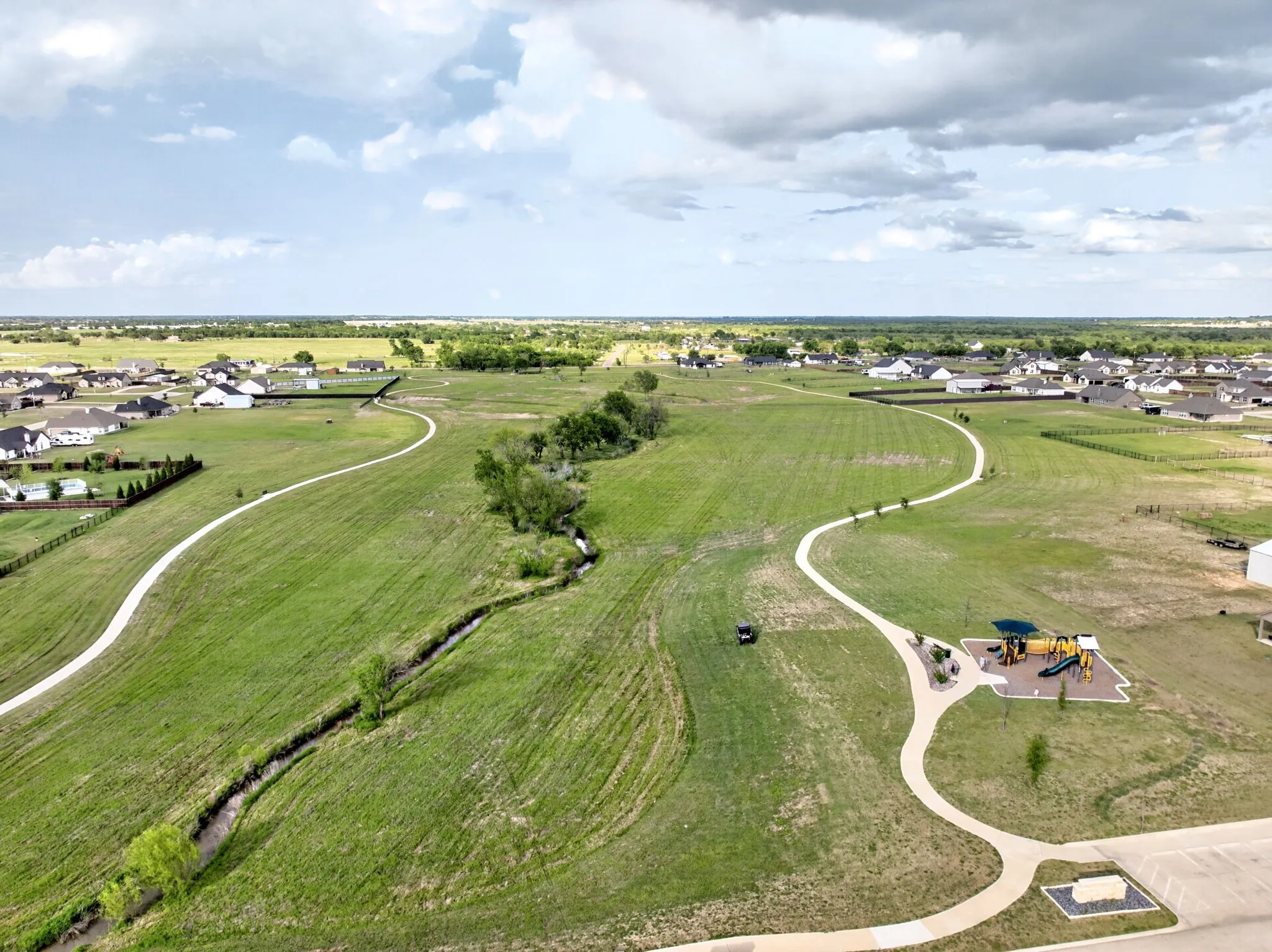 Expansive green spaces featuring a winding pedestrian pathway, a natural drainage creek, and a dedicated play area with equipment