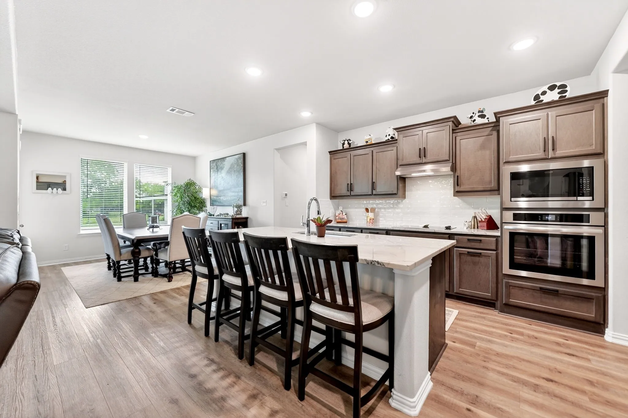 Spacious kitchen featuring an island with seating, stainless steel appliances, wood-finish flooring, recessed lighting, and a white tile backsplash