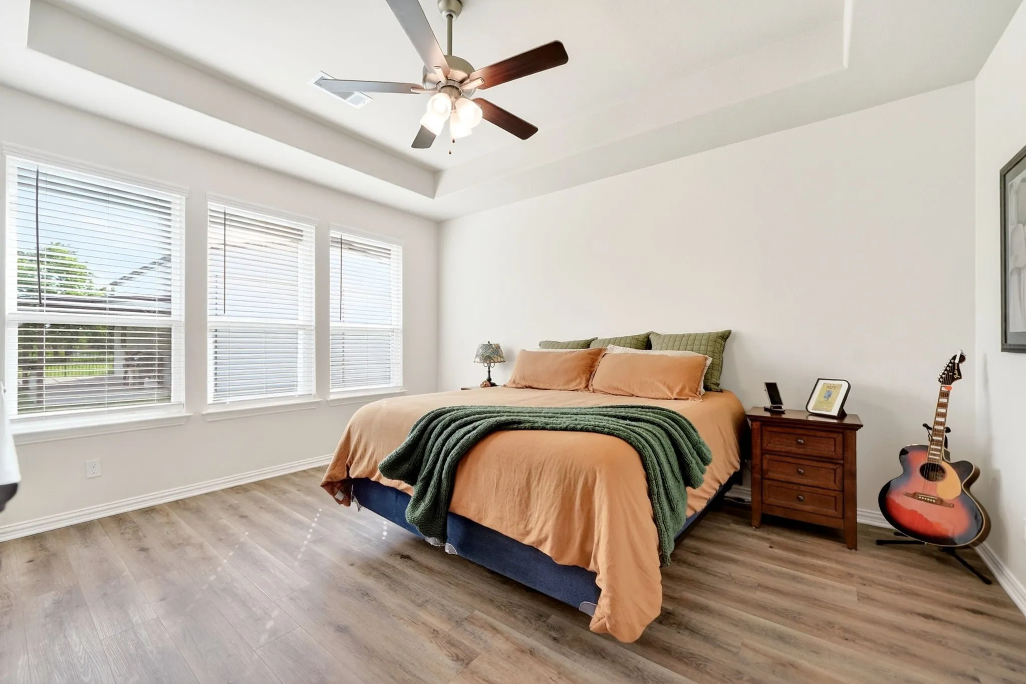 Spacious bedroom featuring wood-finish flooring, a tray ceiling, and a ceiling fan with integrated lighting