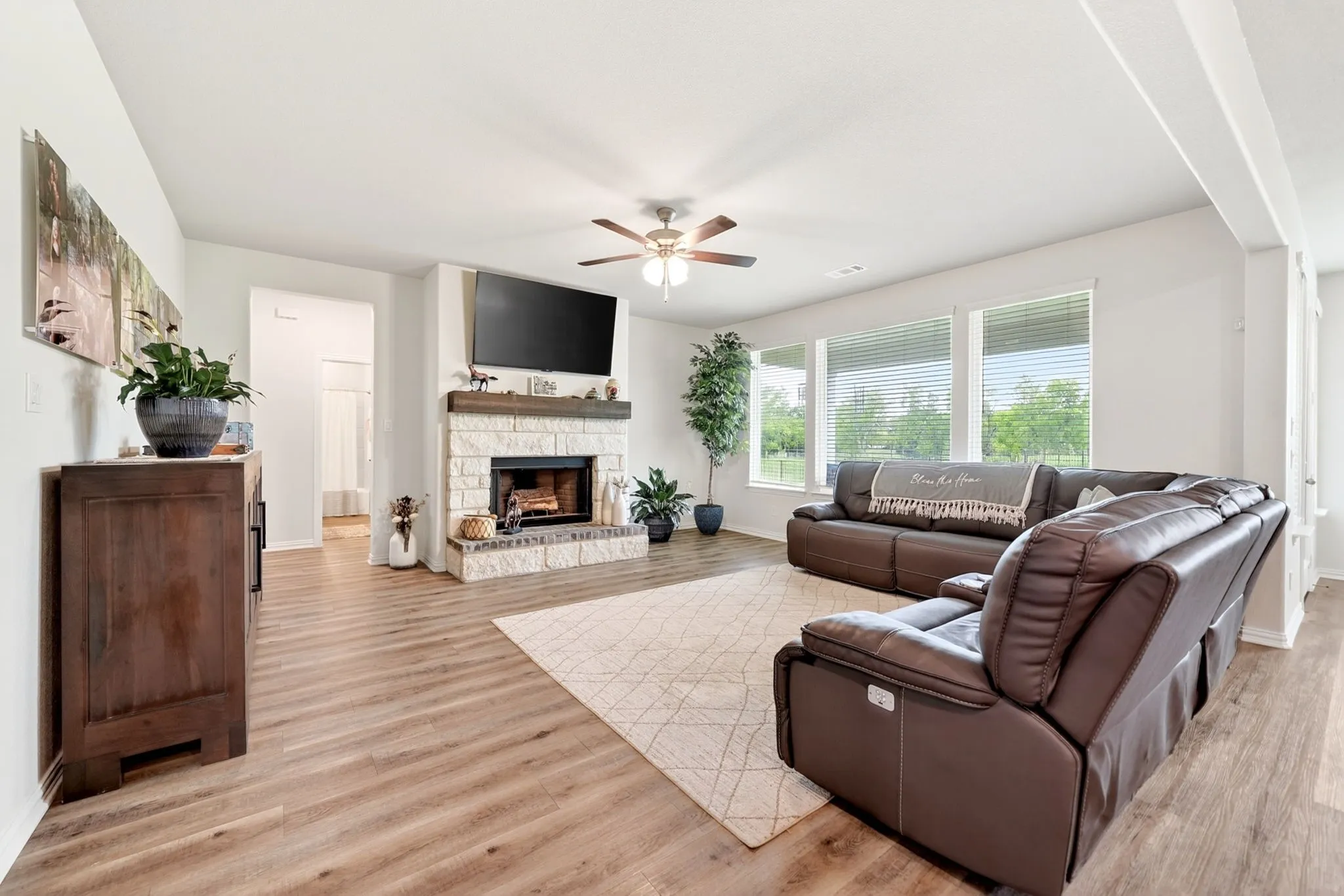 Spacious living area featuring light wood-finish flooring, a stone-faced fireplace with a wood mantel, and a ceiling fan