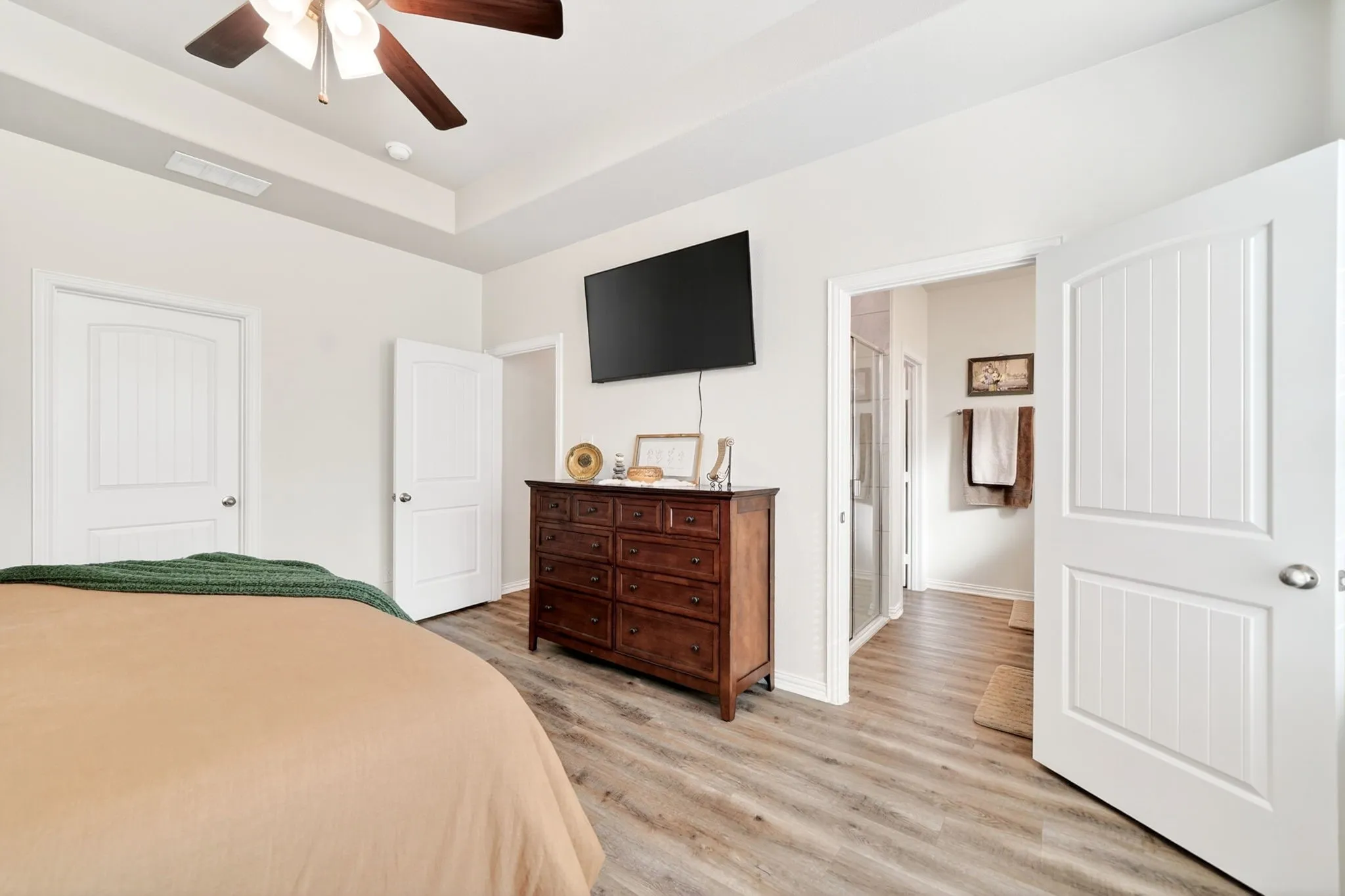 Spacious room with wood-finish flooring, a tray ceiling, and a ceiling fan with integrated lighting