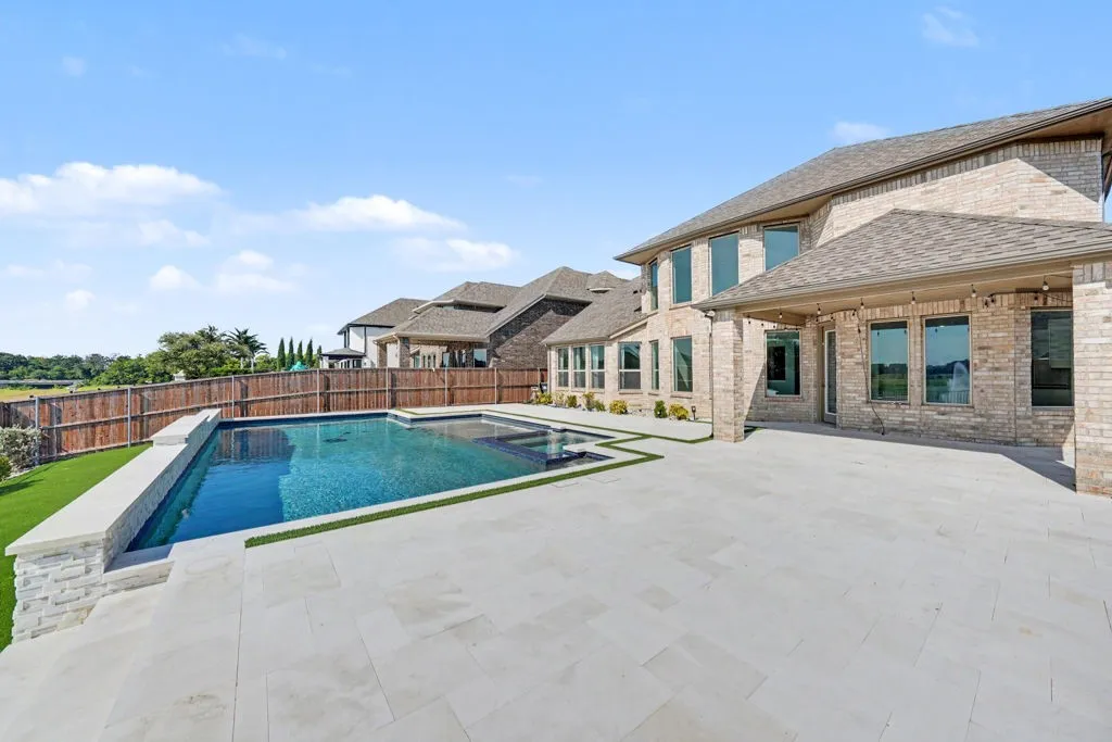 Brick exterior, stone-accented pool, expansive patio, covered outdoor living space, and wood fence