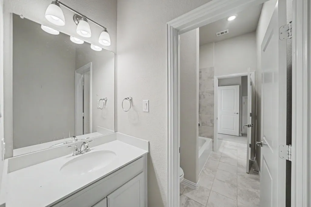 Vanity with integrated sink, polished chrome faucet, rectangular mirror, three-light vanity fixture, and tile flooring