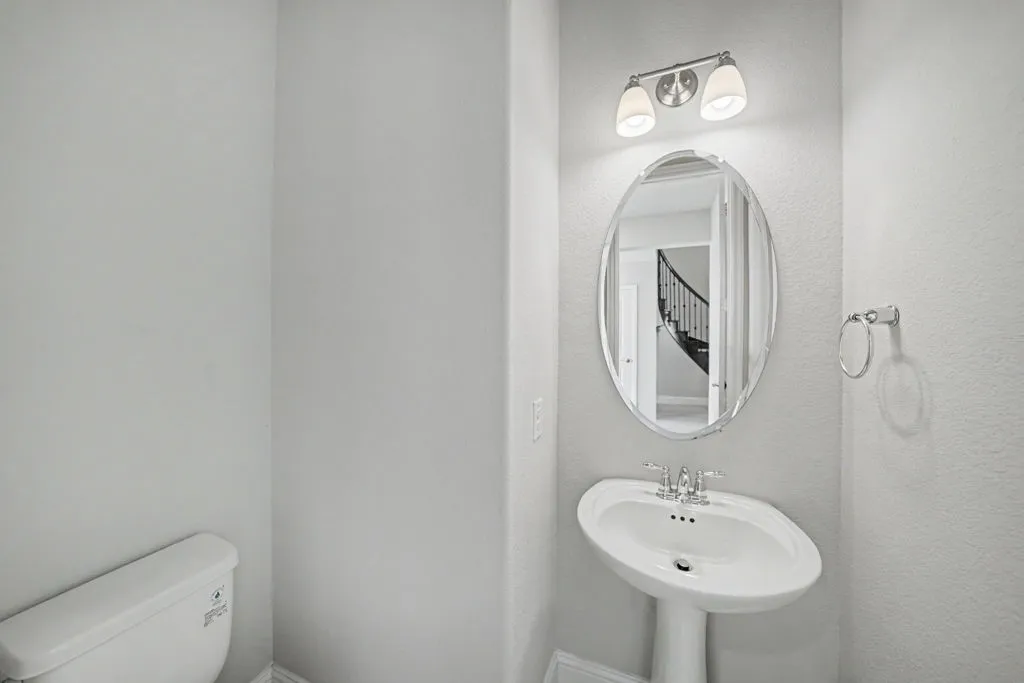 Pedestal sink with chrome fixtures, oval mirror, and a wall-mounted light fixture