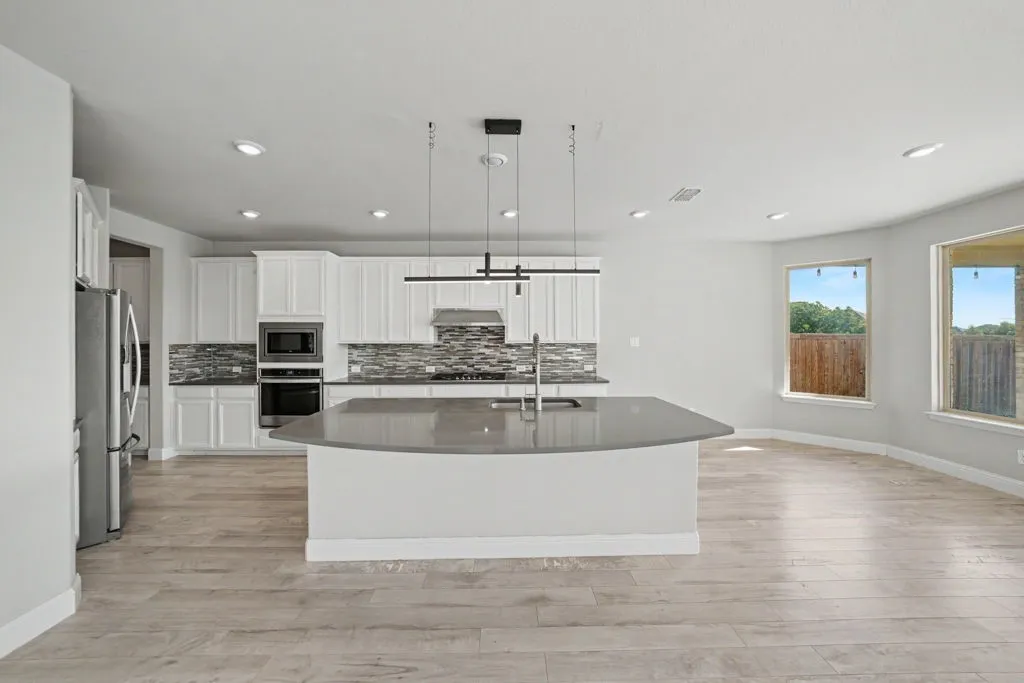 Open-concept kitchen with a large central island, white cabinetry, integrated stainless steel appliances, and wood-finish flooring