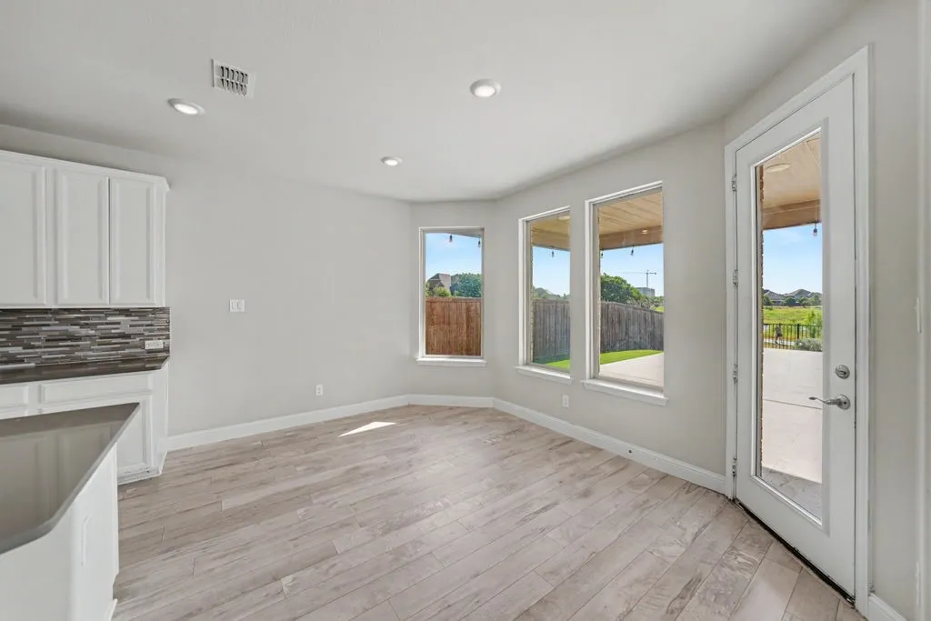 Wood-finish flooring, recessed lighting, white cabinetry, mosaic tile backsplash, and a glass-paneled exterior door