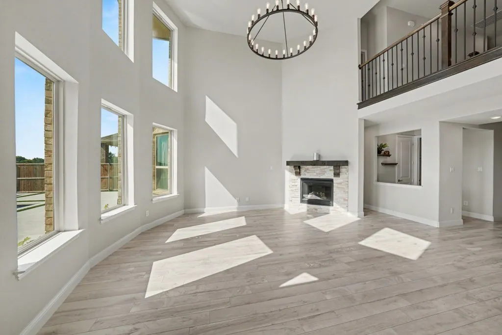 Two-story living area featuring a stacked stone fireplace with a substantial wood mantel, a large round chandelier, and a second-story interior balcony with wrought iron balusters
