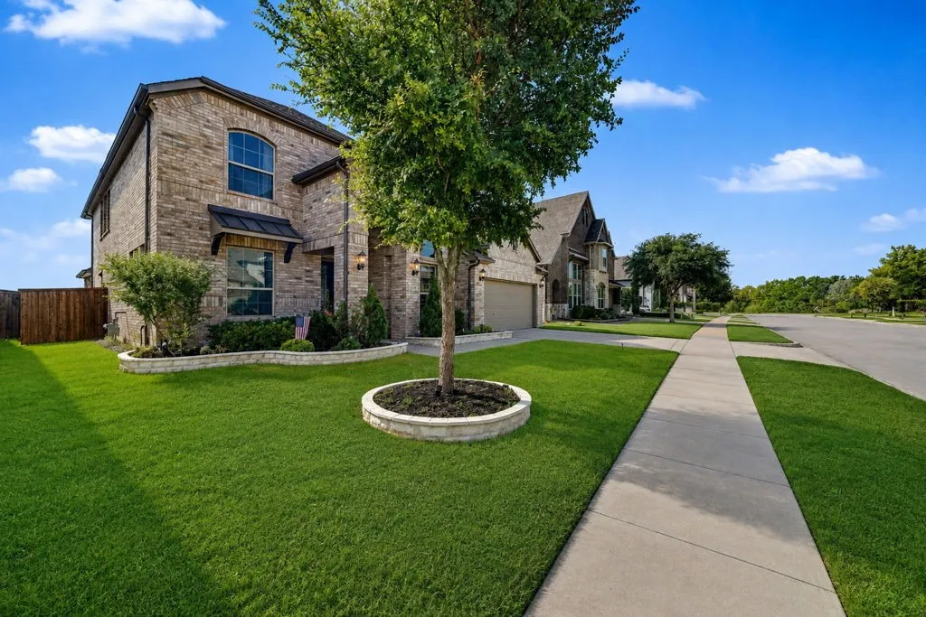 Brick exterior with arched window, front landscaping with stone borders, attached two-car garage, and a concrete sidewalk