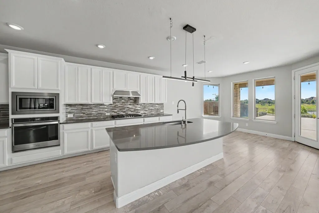 Modern kitchen featuring white cabinetry, stainless steel appliances, a center island with sink, contemporary pendant lighting, and wood-finish flooring