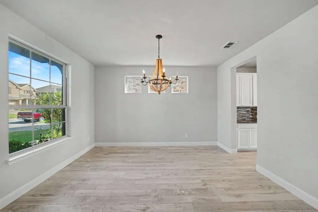 Light wood-finish flooring, a contemporary chandelier, large picture window, and a light color palette