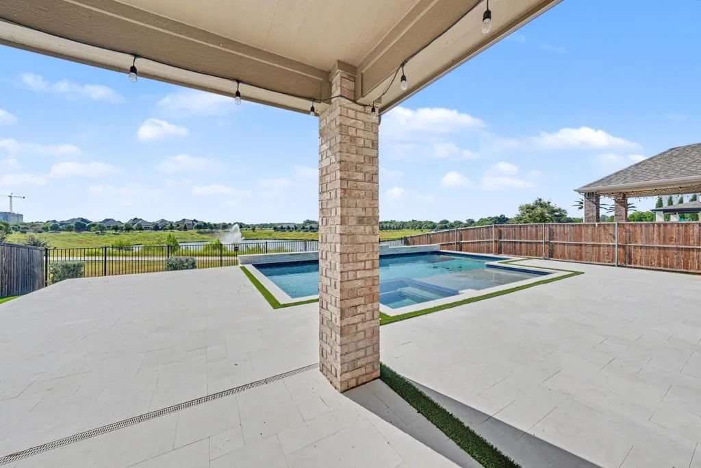 Covered patio with string lighting, brick column, large format tile flooring, and integrated swimming pool
