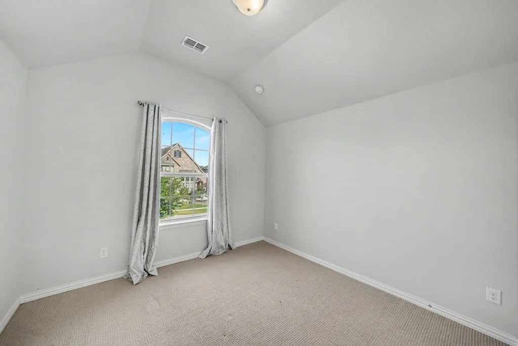 Vaulted ceiling, arched window, neutral wall paint, and light-toned carpet
