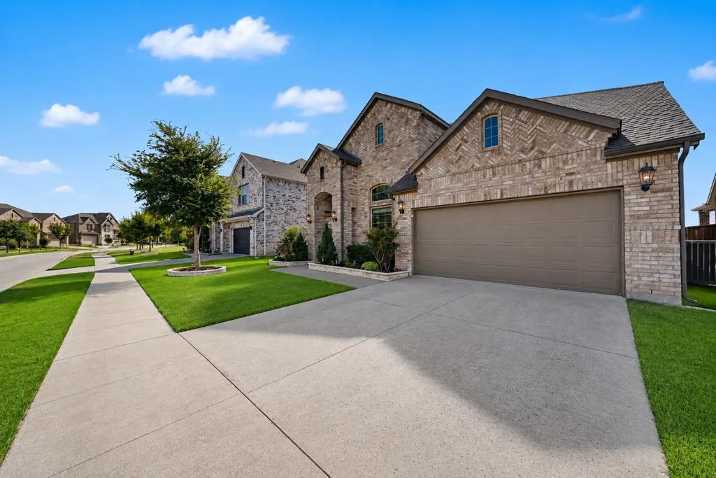 Brick exterior with arched entry, attached garage, concrete driveway, and manicured landscaping