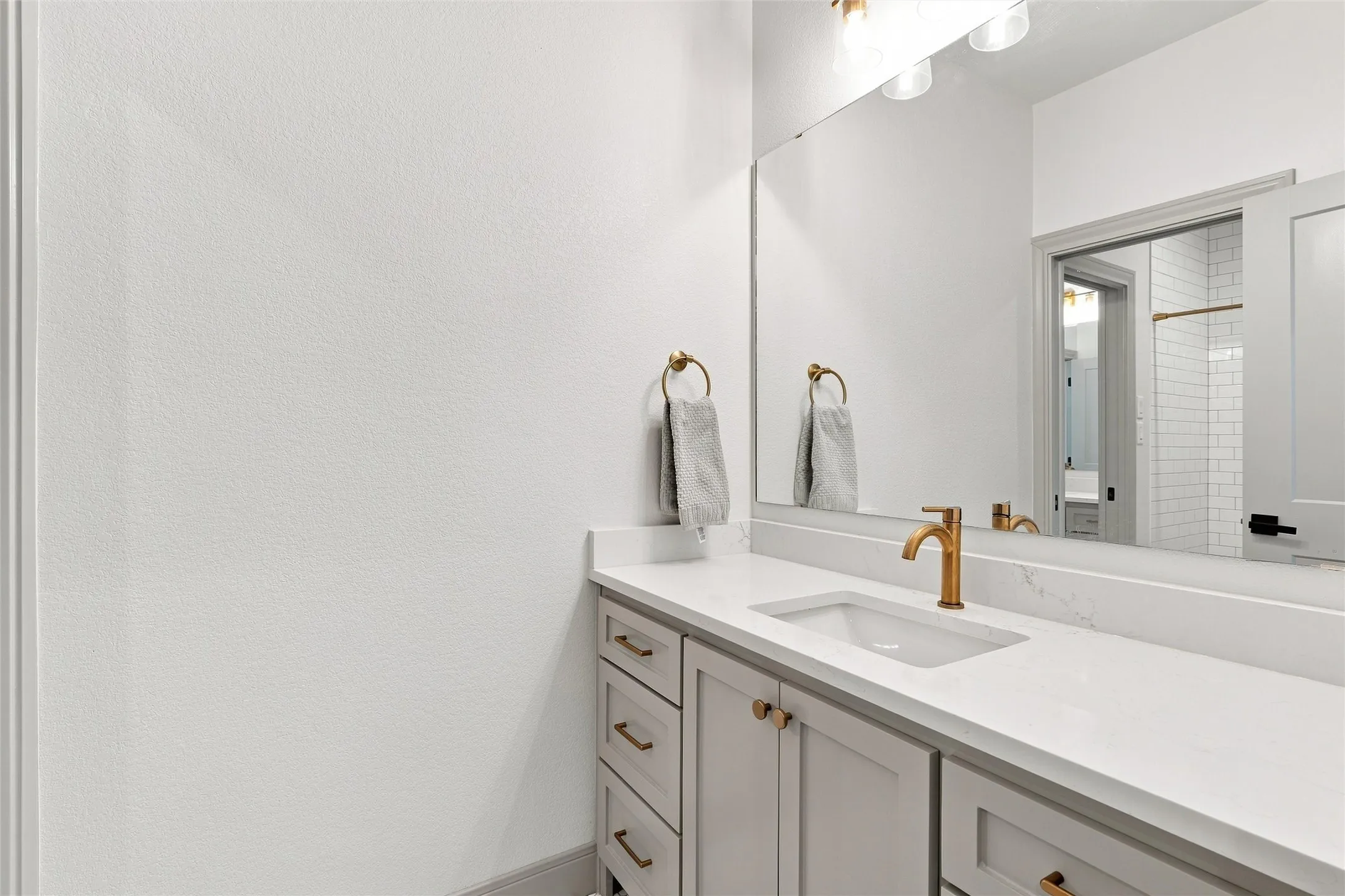 Bathroom vanity featuring a light gray cabinet base, white countertop with integrated sink, brass-finish faucet, and a large wall-mounted mirror