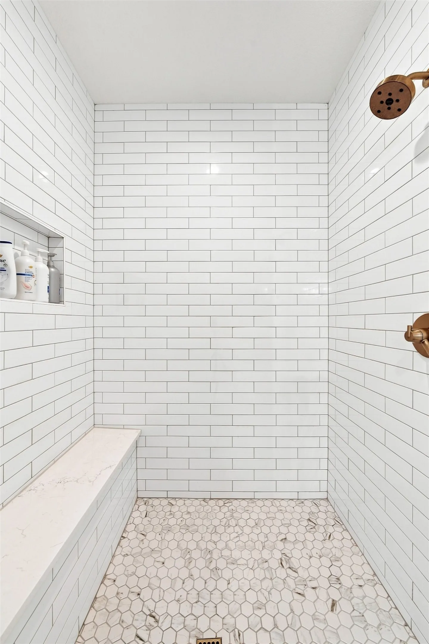 Shower enclosure featuring white subway tile walls, a white hexagonal tile floor, and a built-in bench with a light-toned countertop