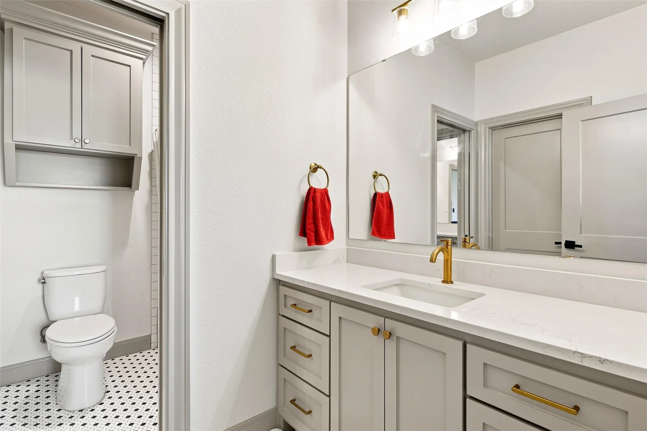 Bathroom vanity featuring a light-toned countertop, undermount sink with a brass-finish faucet, and coordinating brass-finish hardware on cabinetry
