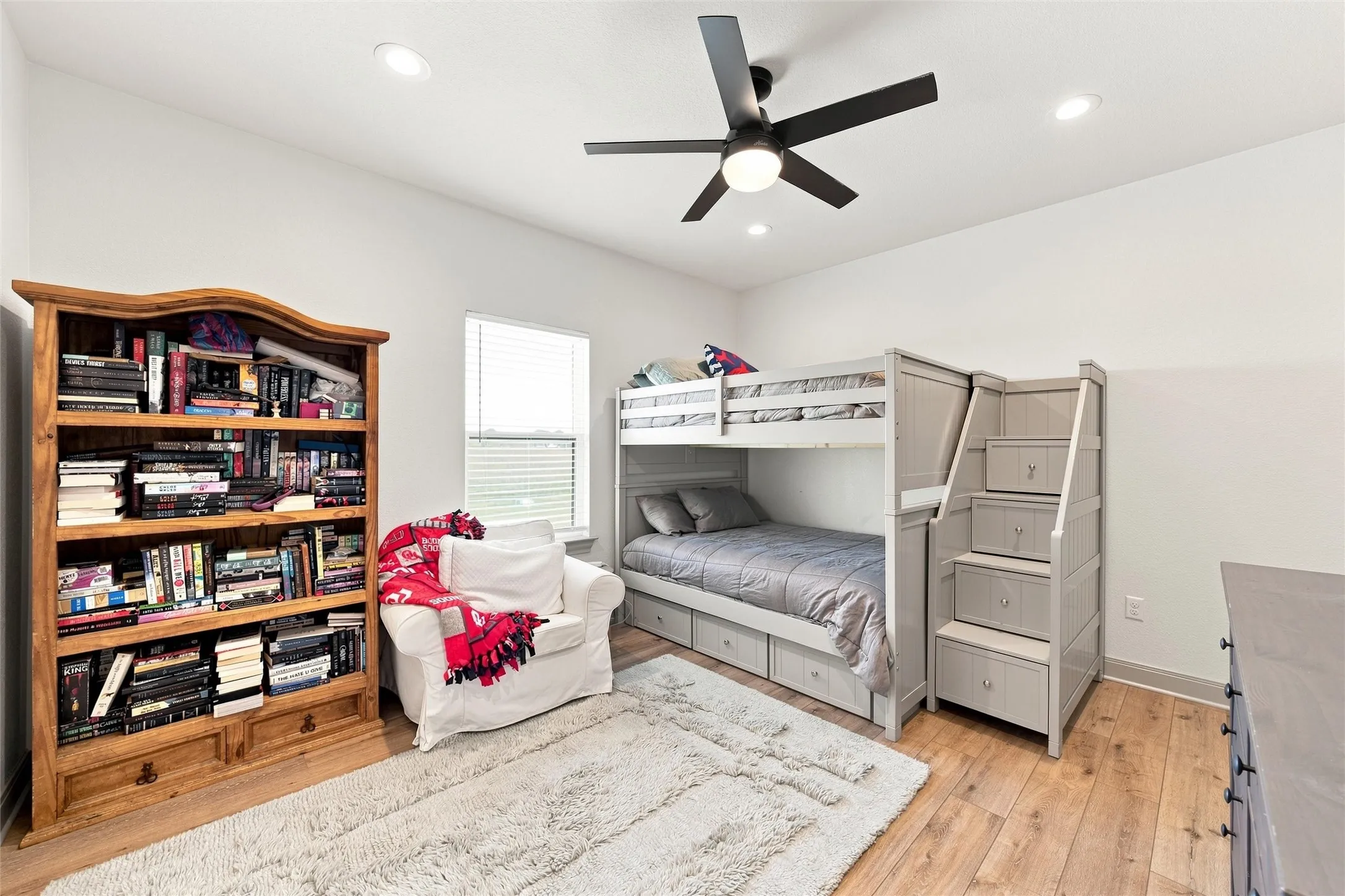 Spacious room featuring wood-finish flooring, a built-in bunk bed with integrated storage, and an attached staircase with drawers