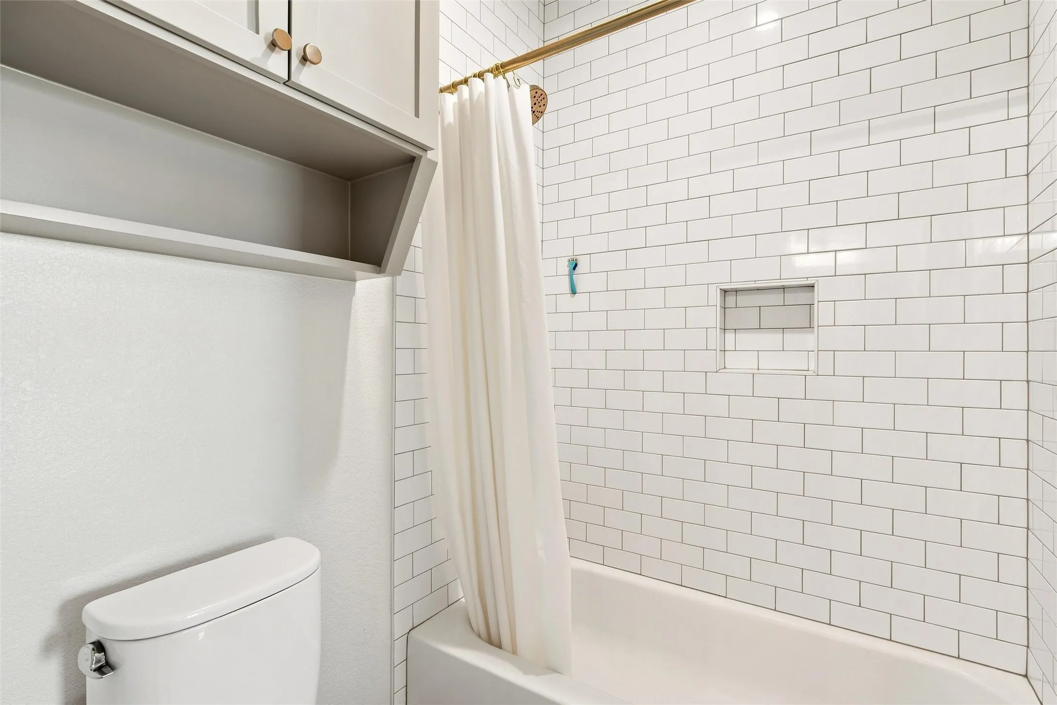 Bathroom featuring white subway tile surround with built-in niche, white bathtub, and gold-finish shower rod