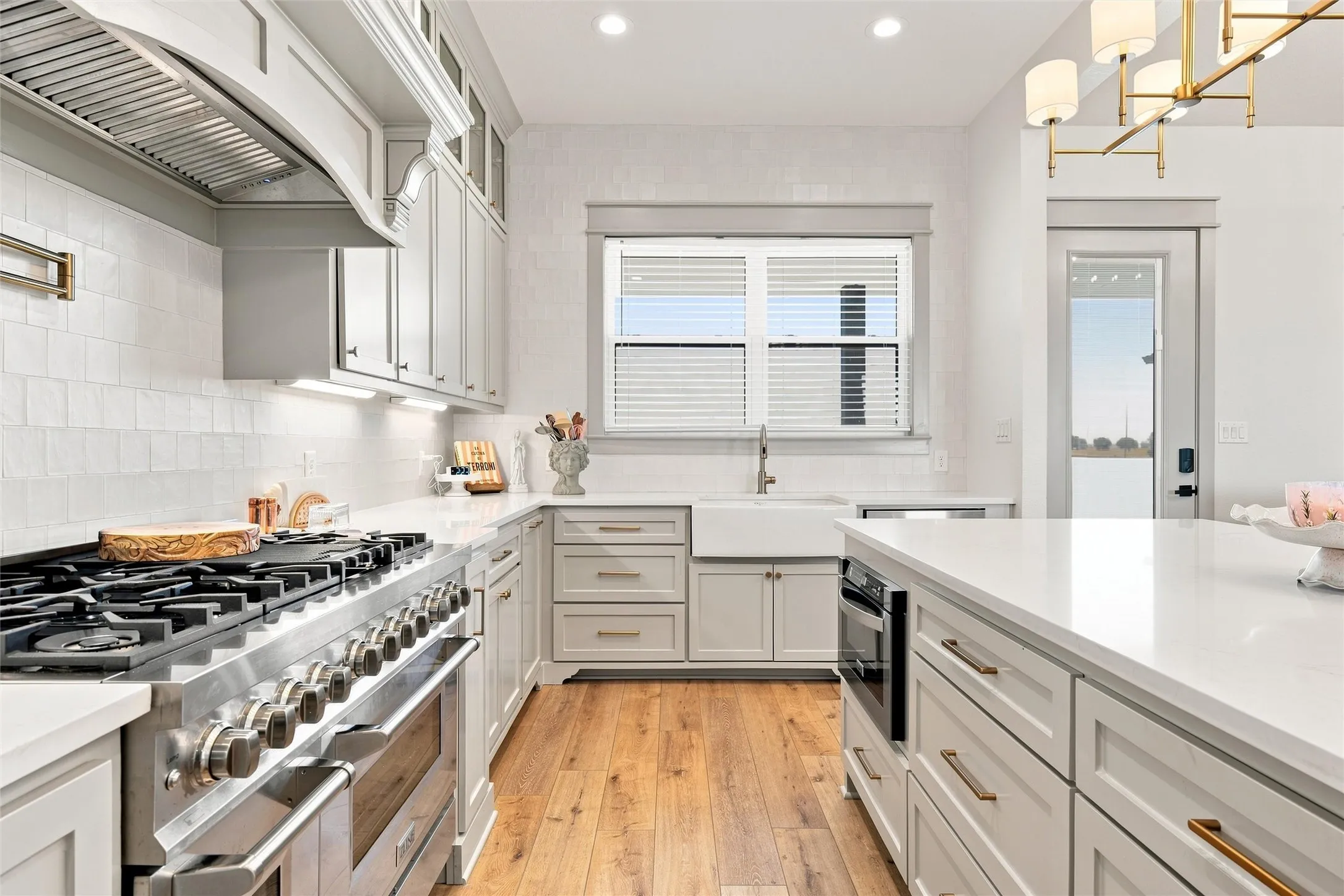Gourmet kitchen featuring a large professional-grade range, custom cabinetry with brushed gold hardware, pristine white countertops, a farmhouse sink, and wood-finish flooring