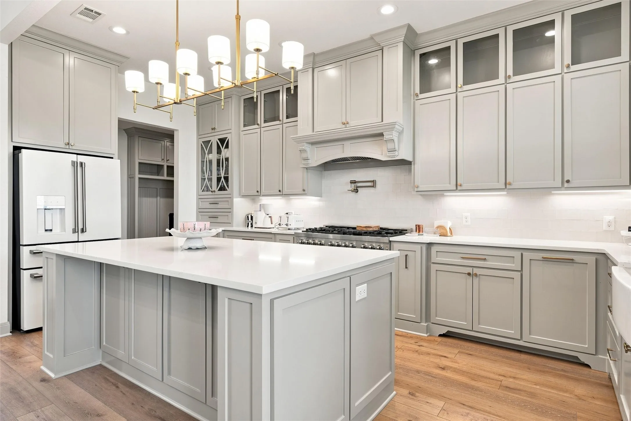 Modern kitchen featuring light gray cabinetry, a central island with a solid surface countertop, wood-finish flooring, a stainless steel range, and a subway tile backsplash