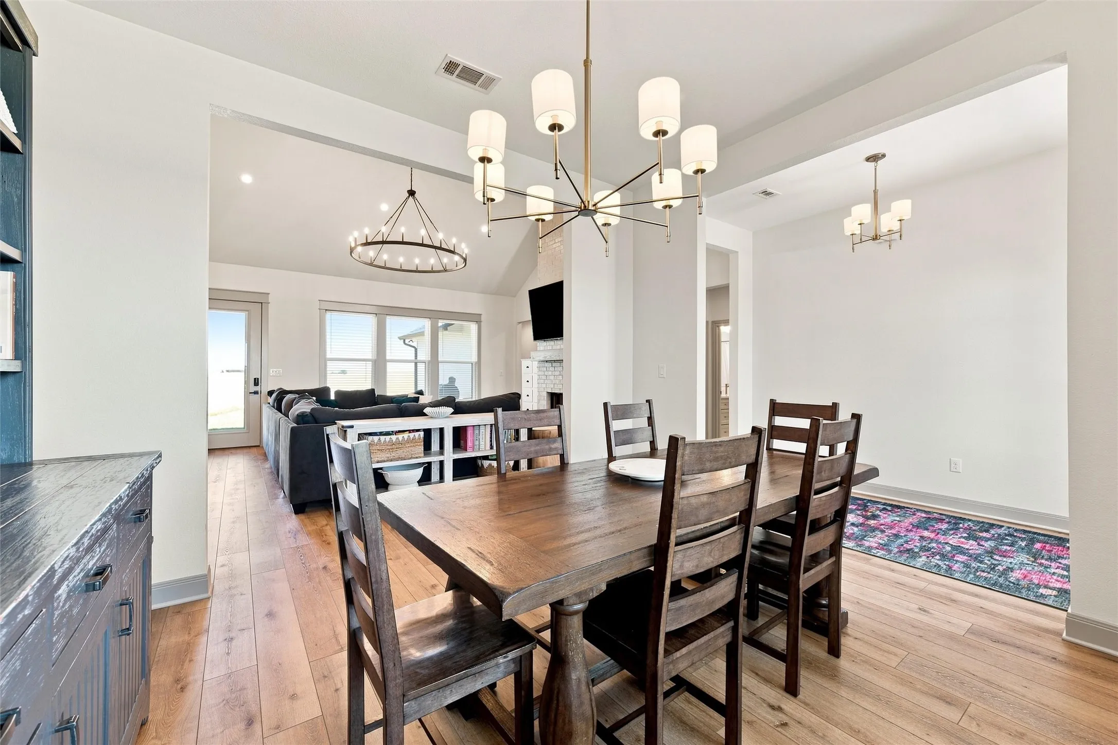 Dining area featuring wood-finish flooring, a modern chandelier with sconce lighting, and a wide entryway to the living area