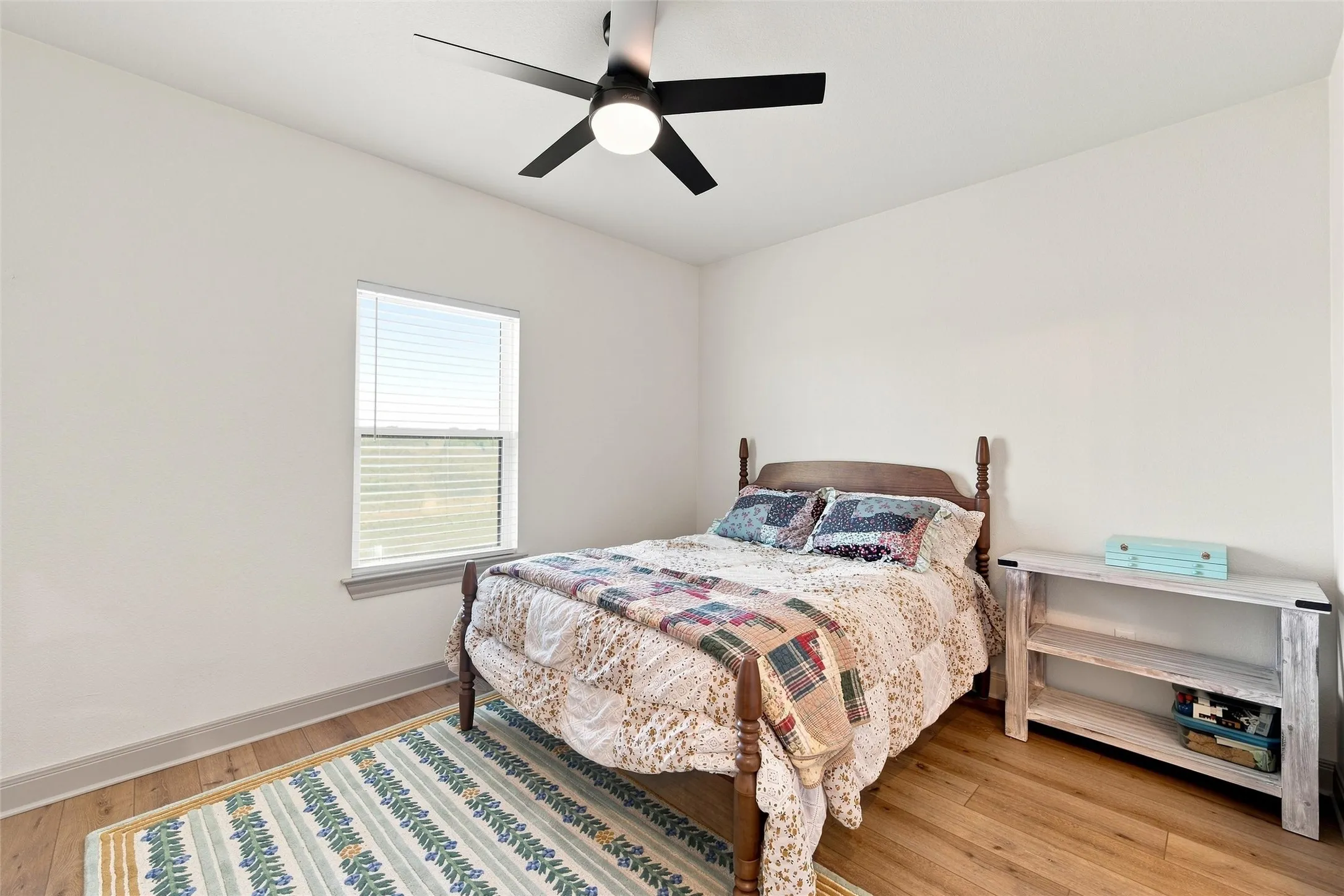 Bright interior space featuring wood-finish flooring, a single window with horizontal blinds, and a ceiling fan with integrated lighting