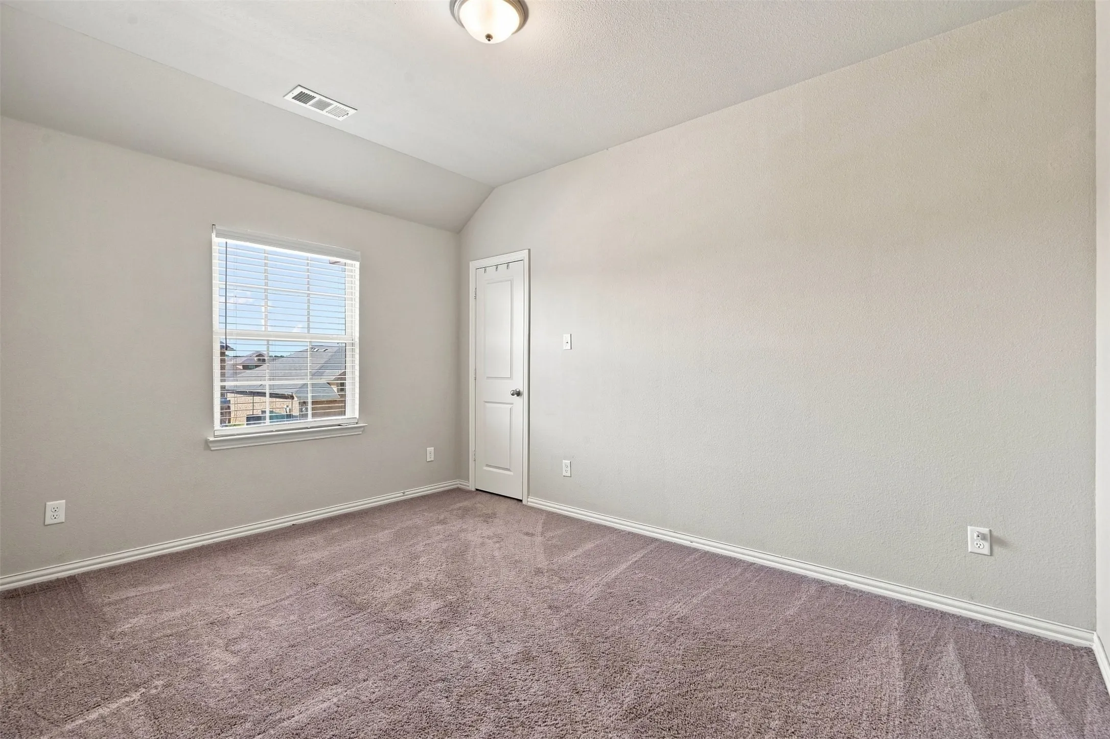 Carpeted room with a vaulted ceiling, a window featuring horizontal blinds, and a paneled door