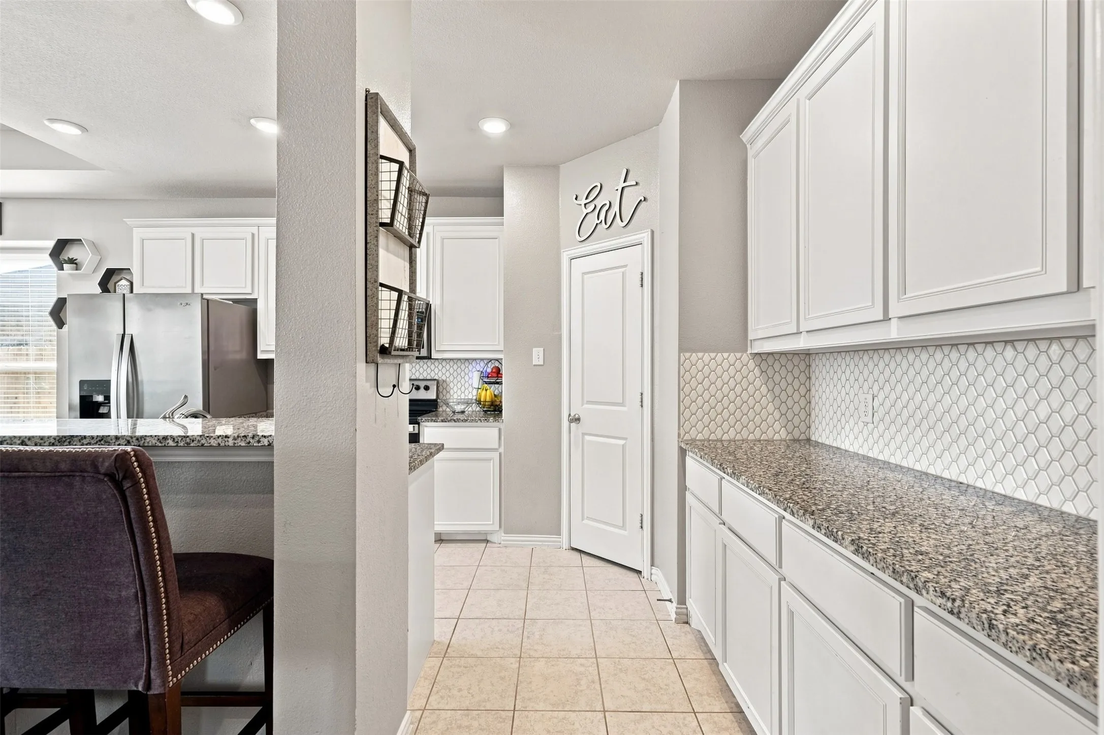 Kitchen featuring white cabinetry with crown molding, light-toned granite countertops, and a white patterned tile backsplash