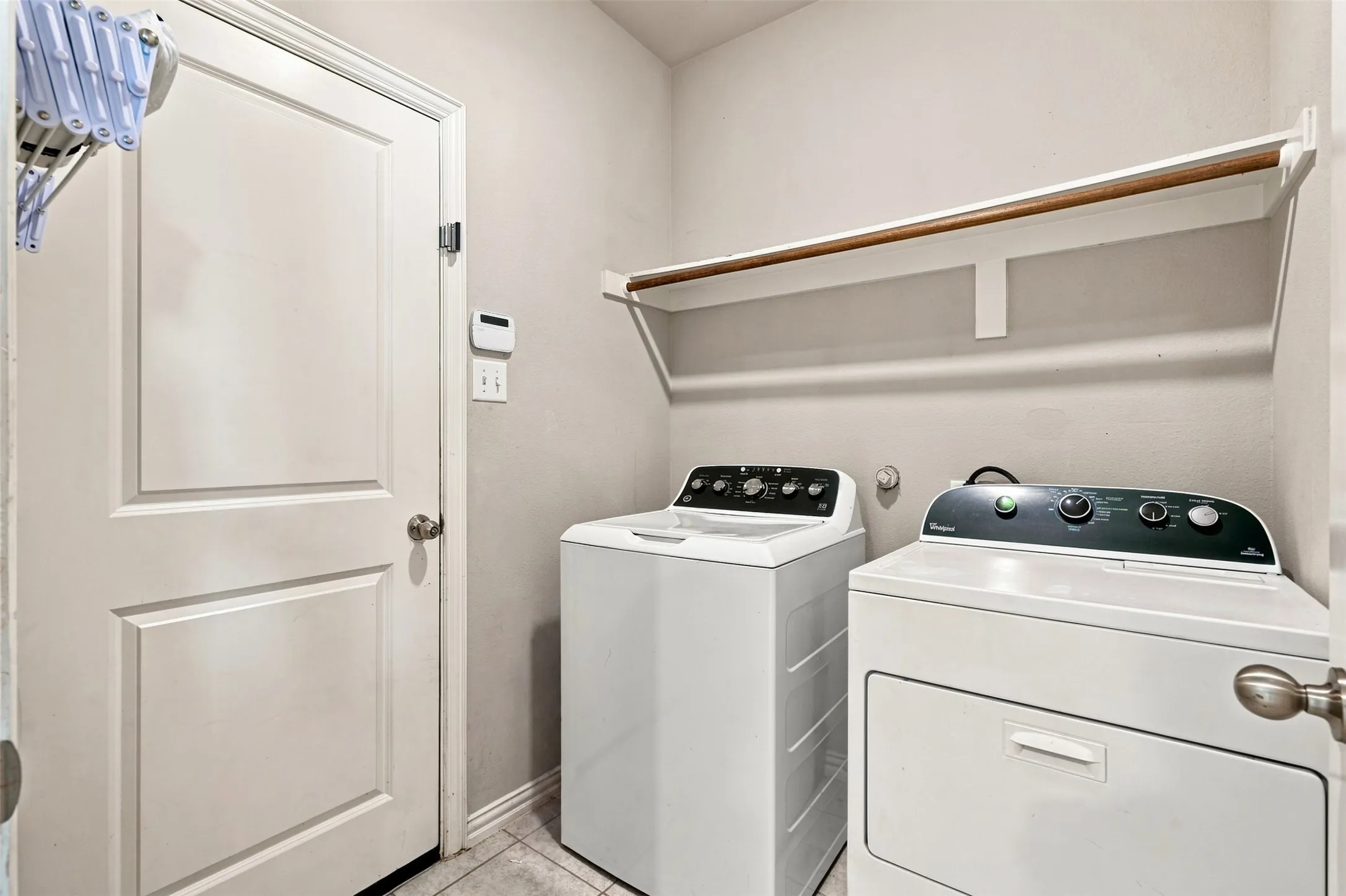 Dedicated laundry area featuring a white paneled door, light-toned walls, and a built-in shelving unit with a hanging rod