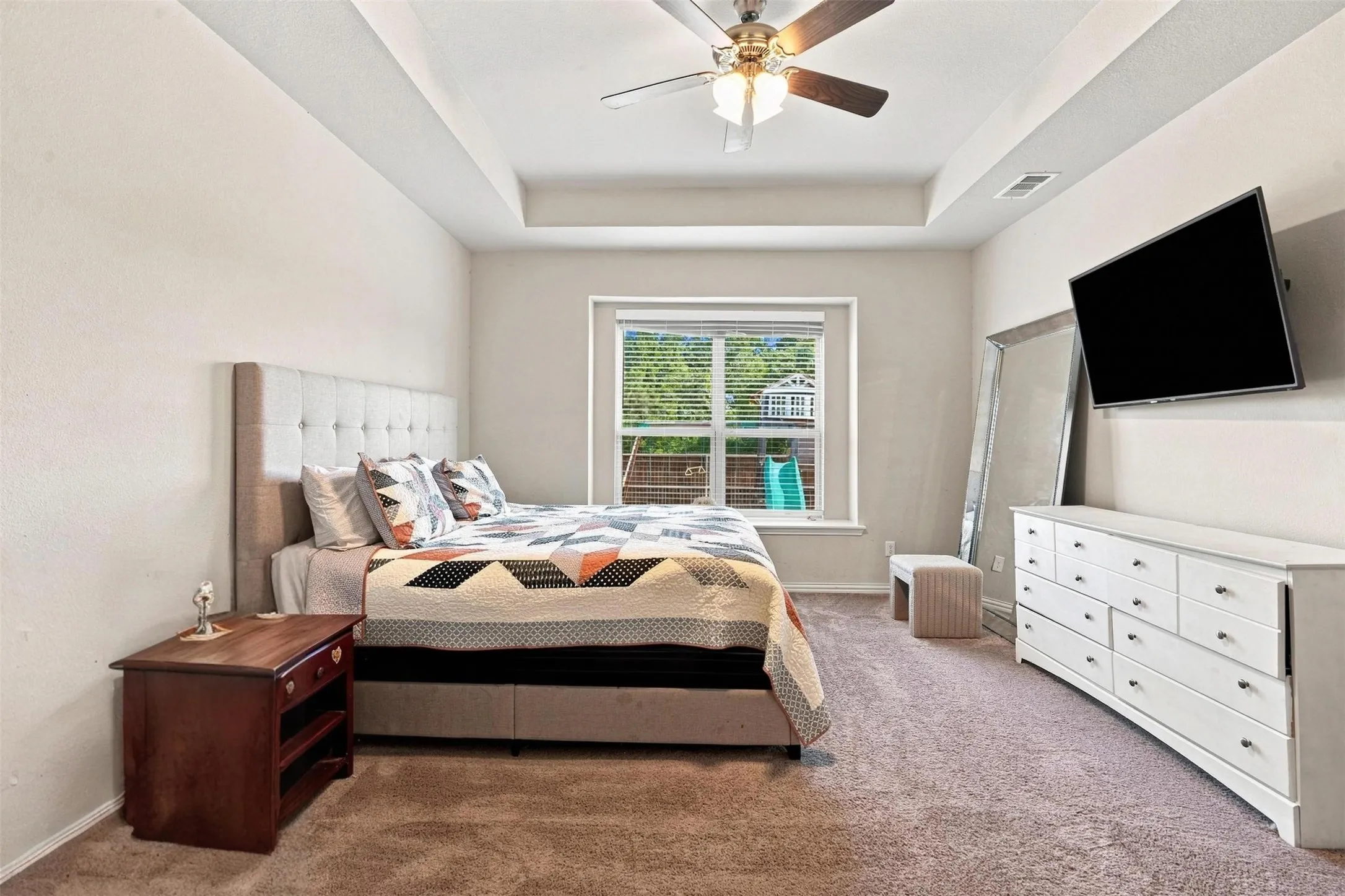 Bedroom featuring a tray ceiling with a ceiling fan, neutral carpet flooring, and a large window with horizontal blinds