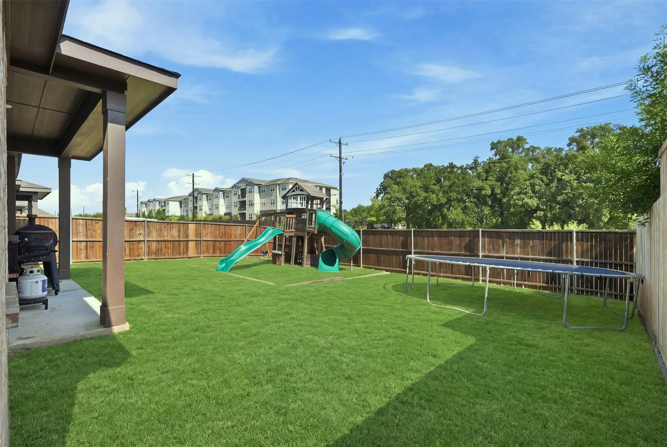 Expansive rear yard featuring a covered patio, manicured lawn, and wooden privacy fencing