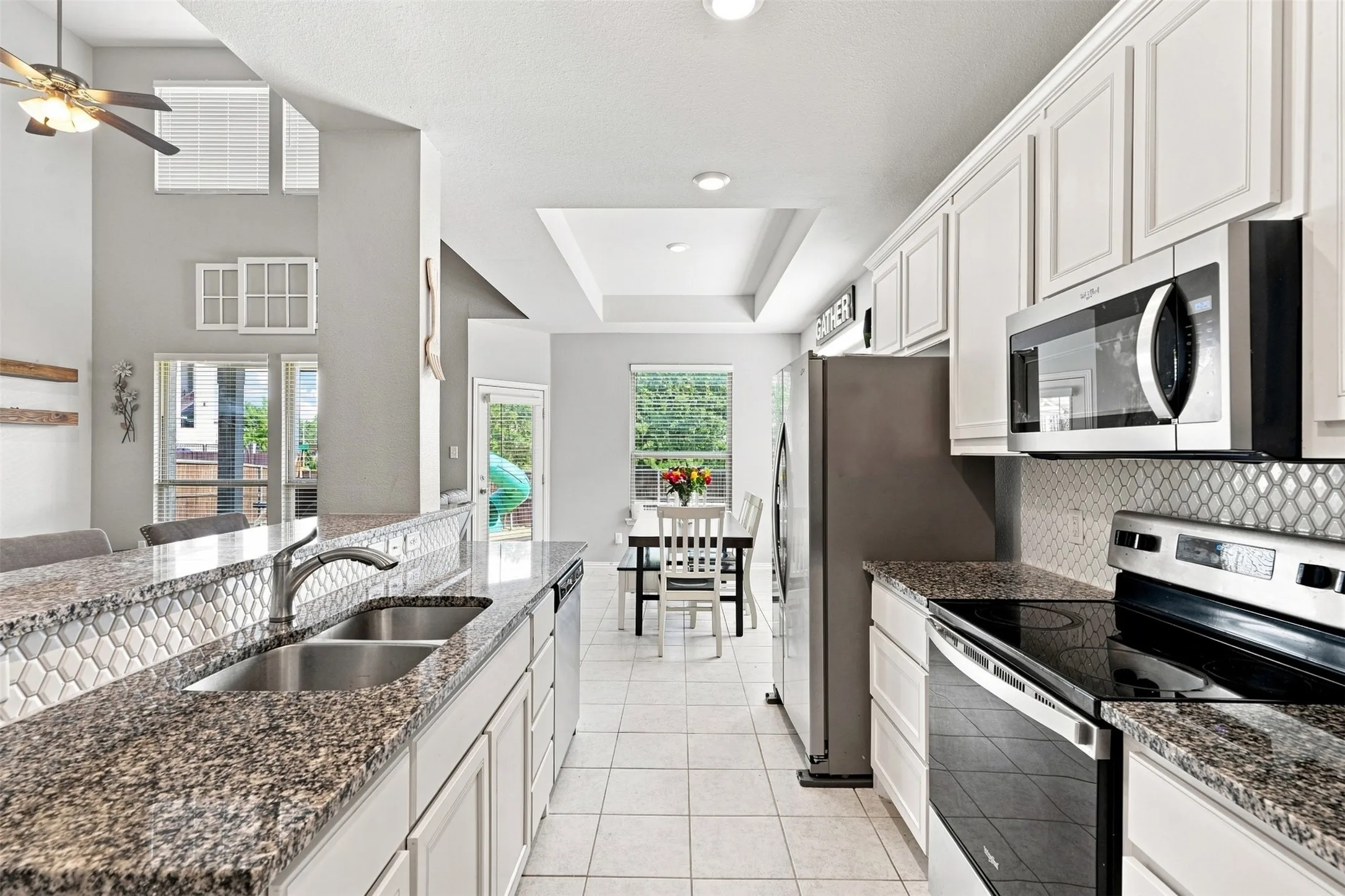Kitchen featuring granite countertops, stainless steel appliances, white cabinetry, and a mosaic tile backsplash