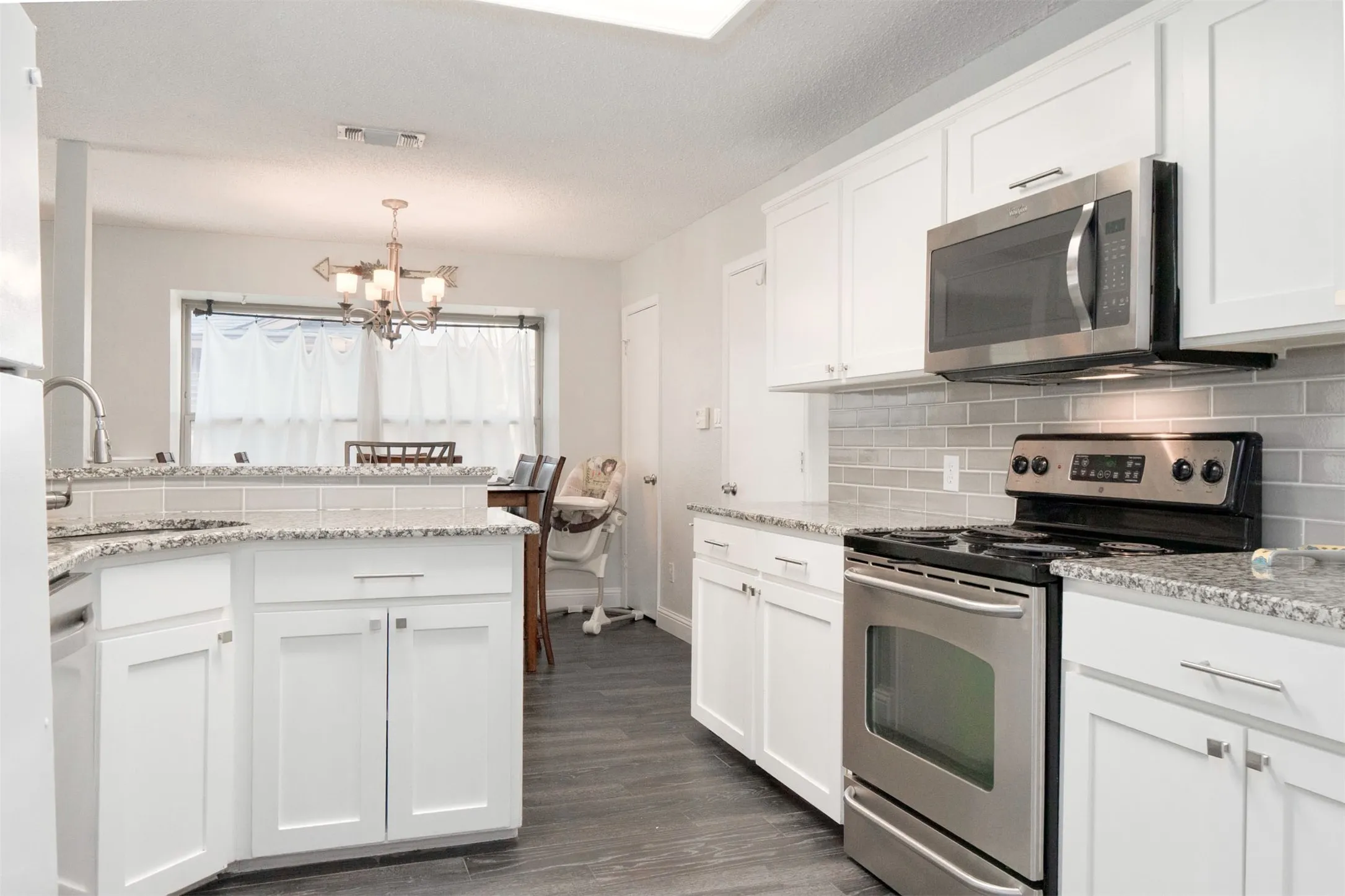 Kitchen featuring white shaker-style cabinetry, stainless steel appliances, granite countertops, and a gray subway tile backsplash
