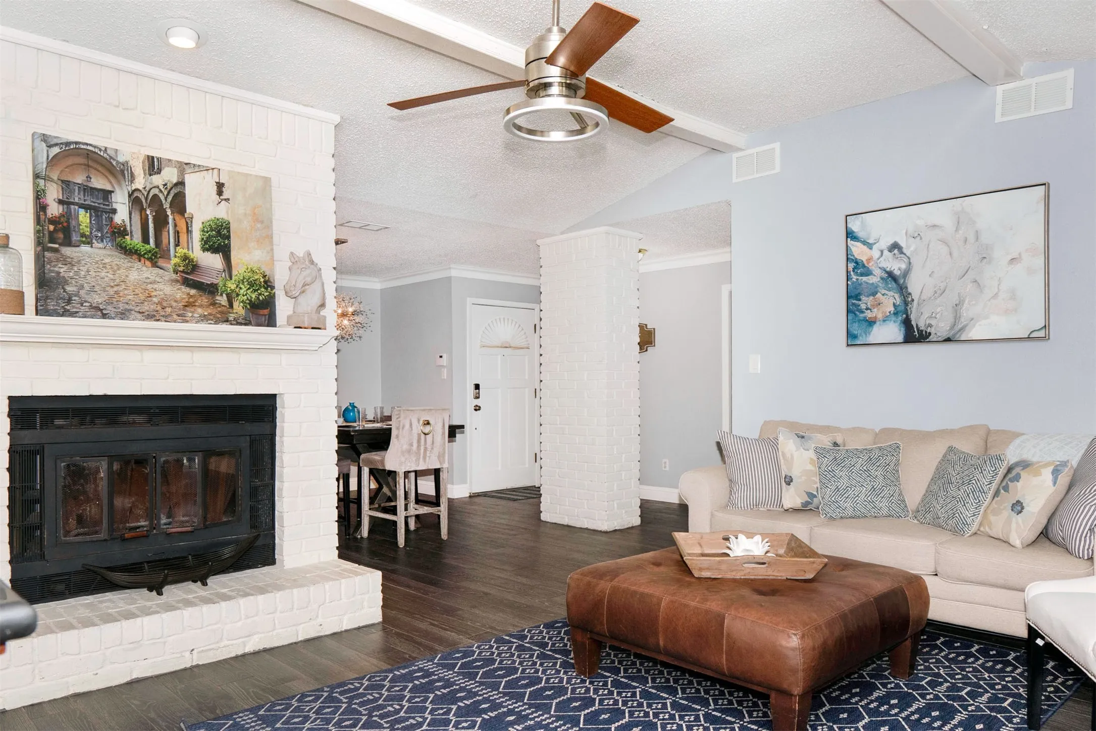 Living area featuring a white-painted brick fireplace with a dark insert, wood-finish flooring, and a vaulted ceiling with exposed white beams