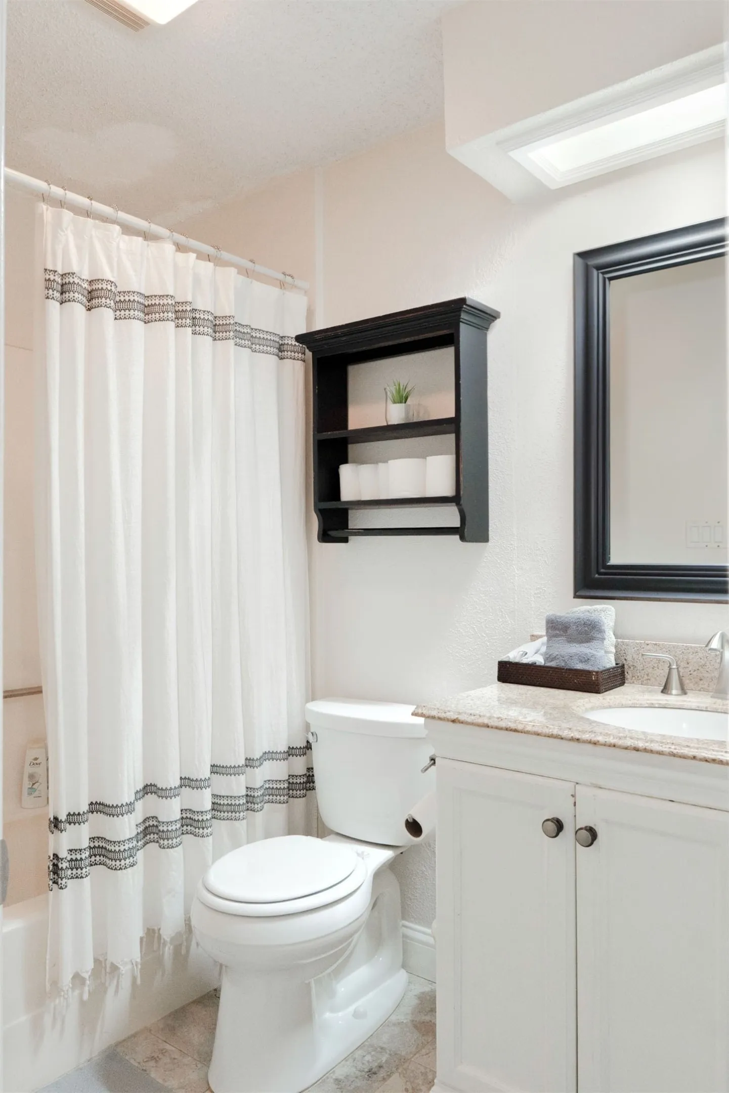 Bathroom featuring a white vanity with a light-toned countertop, a black framed mirror, and a built-in wall shelf