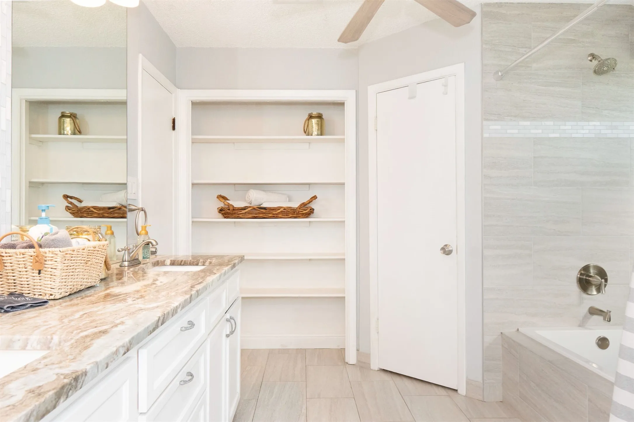 Bathroom featuring a double vanity with a variegated stone countertop, integrated sinks, white cabinetry with silver-tone hardware, and an expansive mirror