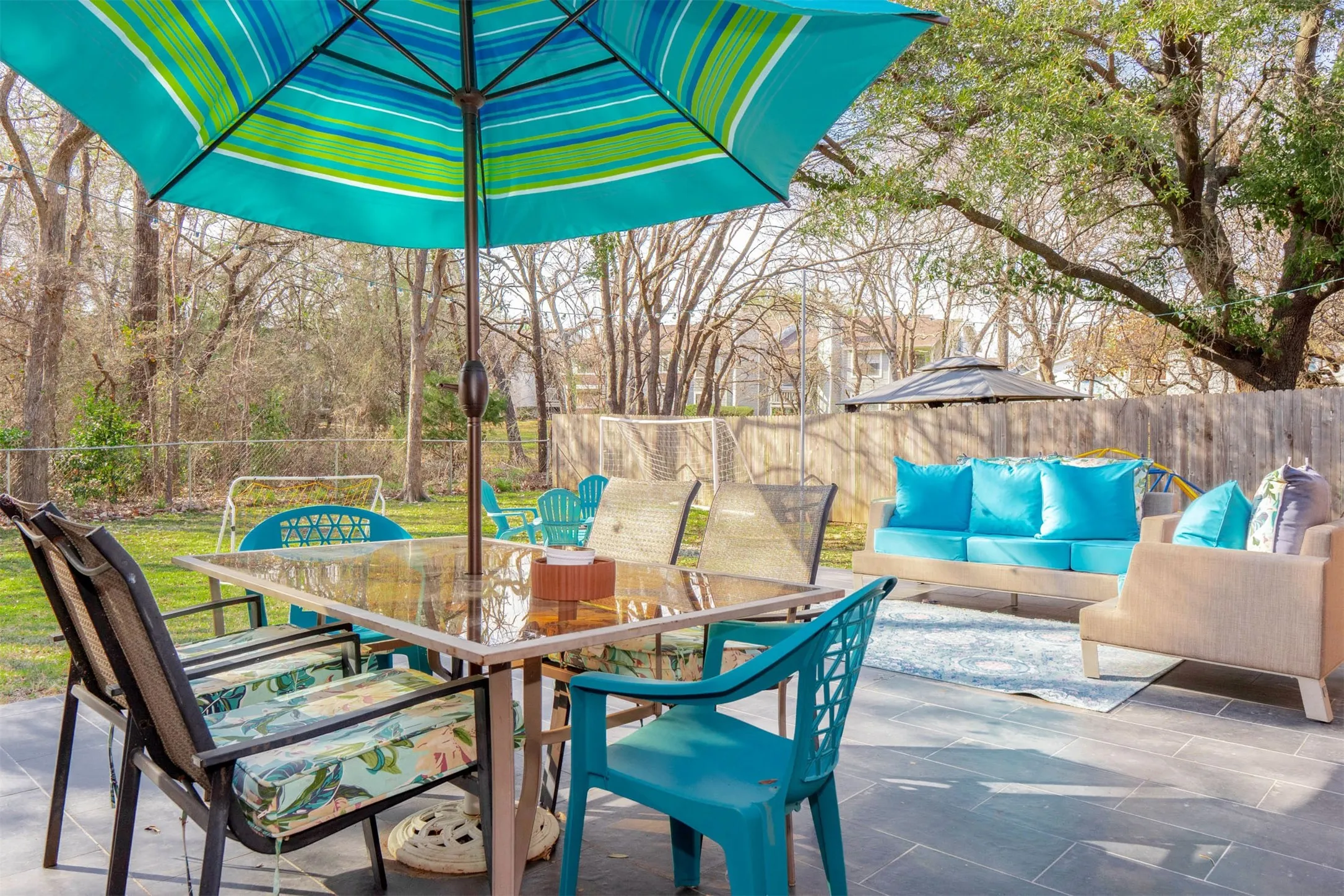 Spacious backyard patio featuring large format tile, a private wood fence, mature trees, and an expansive lawn area