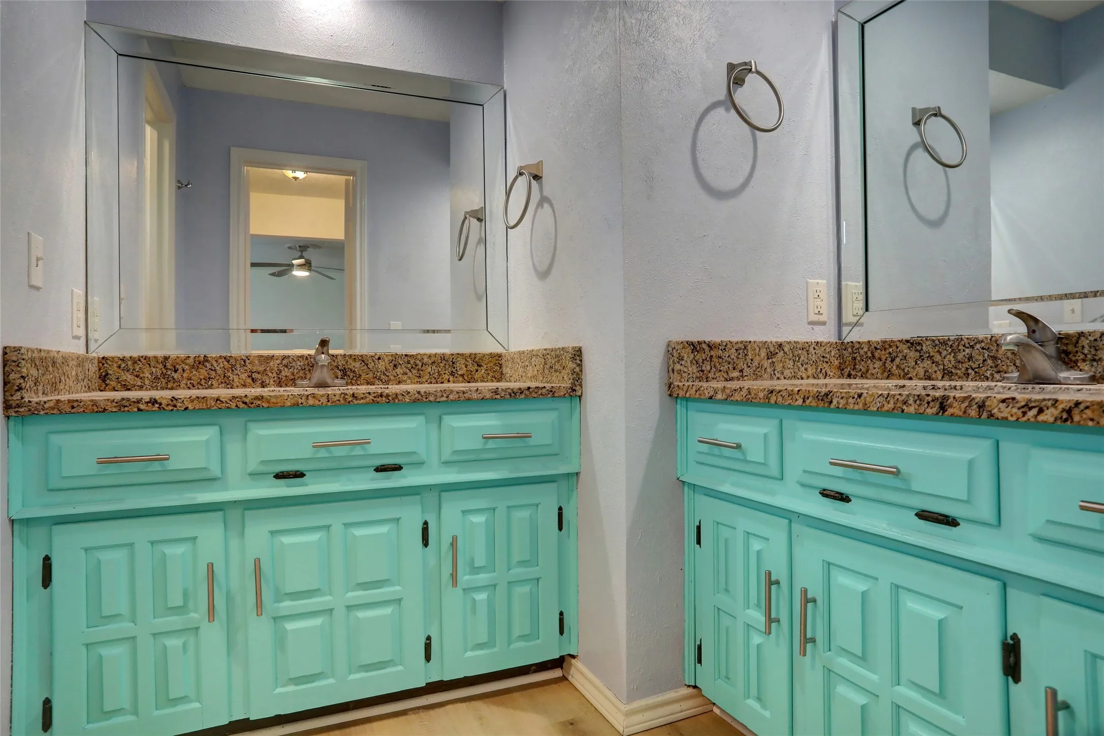 Double vanity featuring teal cabinetry with panel detailing, stone countertops, and individual mirrors