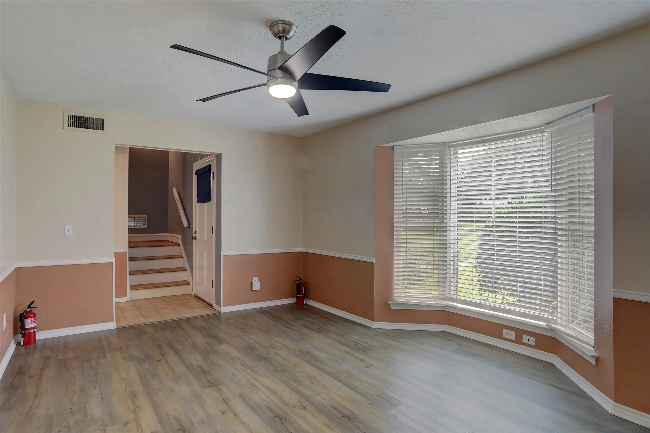 Spacious room featuring wood-finish flooring, a bay window with blinds, and a contemporary ceiling fan