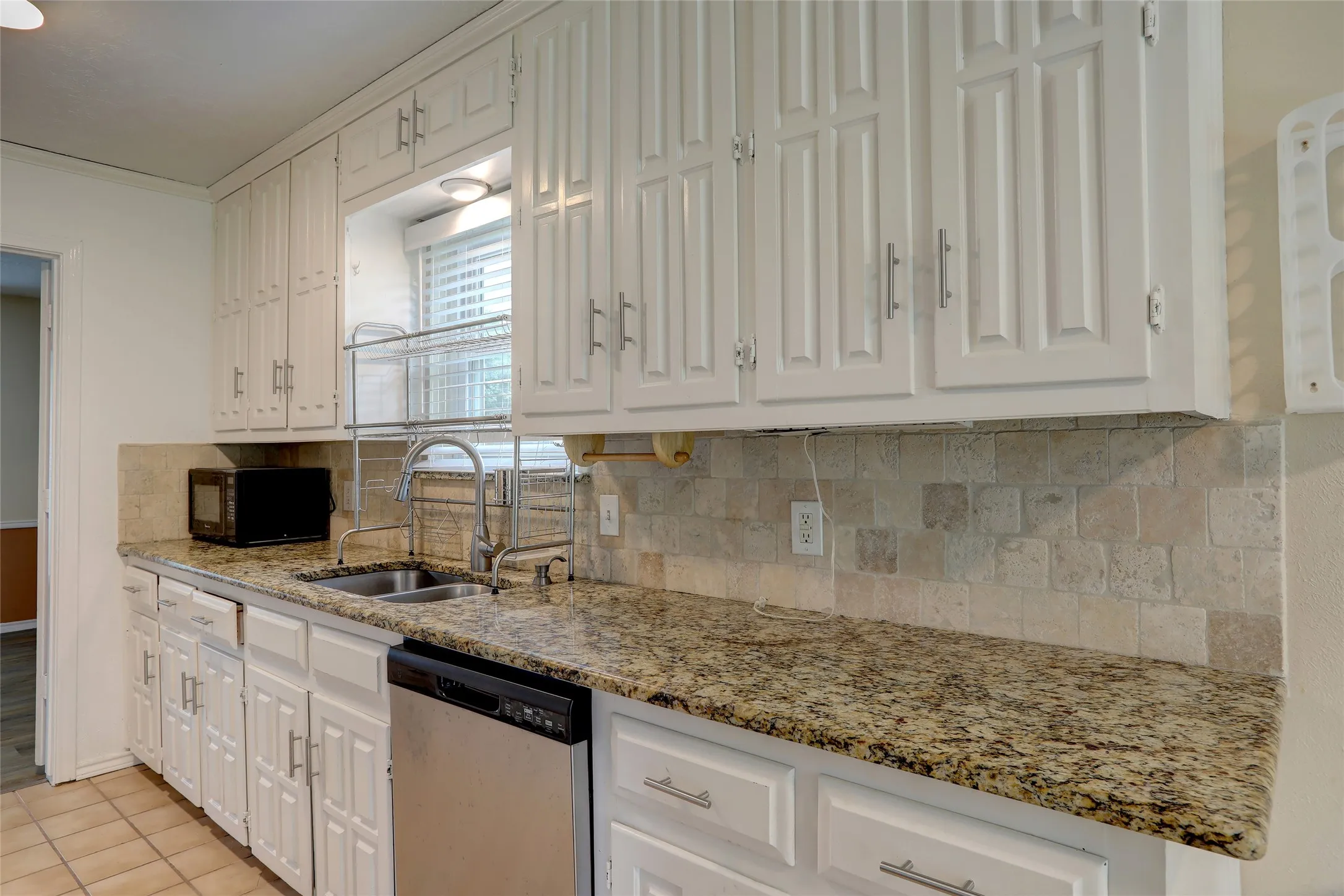 Kitchen featuring white cabinetry, granite-finish countertops, a stone-tile backsplash, and a double basin sink