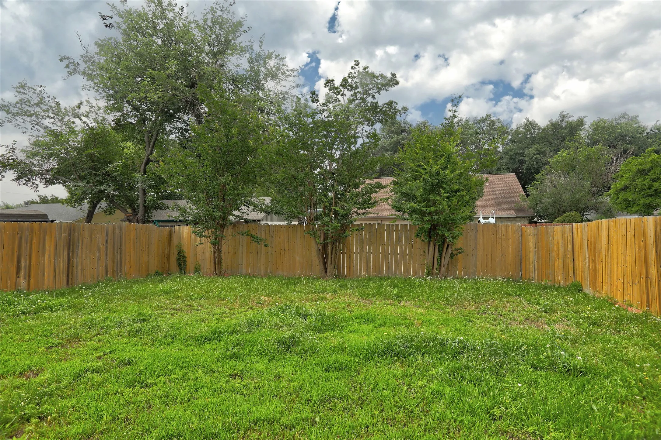 Expansive backyard featuring a wood privacy fence, mature trees, and a grass lawn