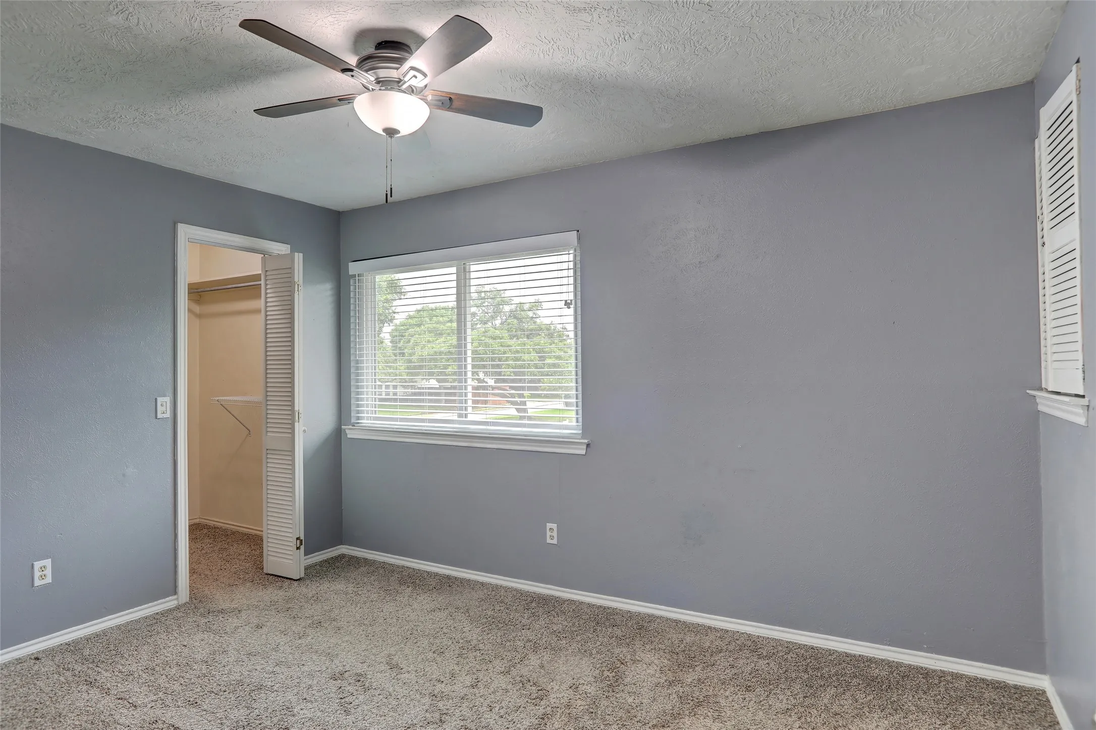 Carpeted room with a ceiling fan, a window featuring blinds, and a closet with bifold louvered doors