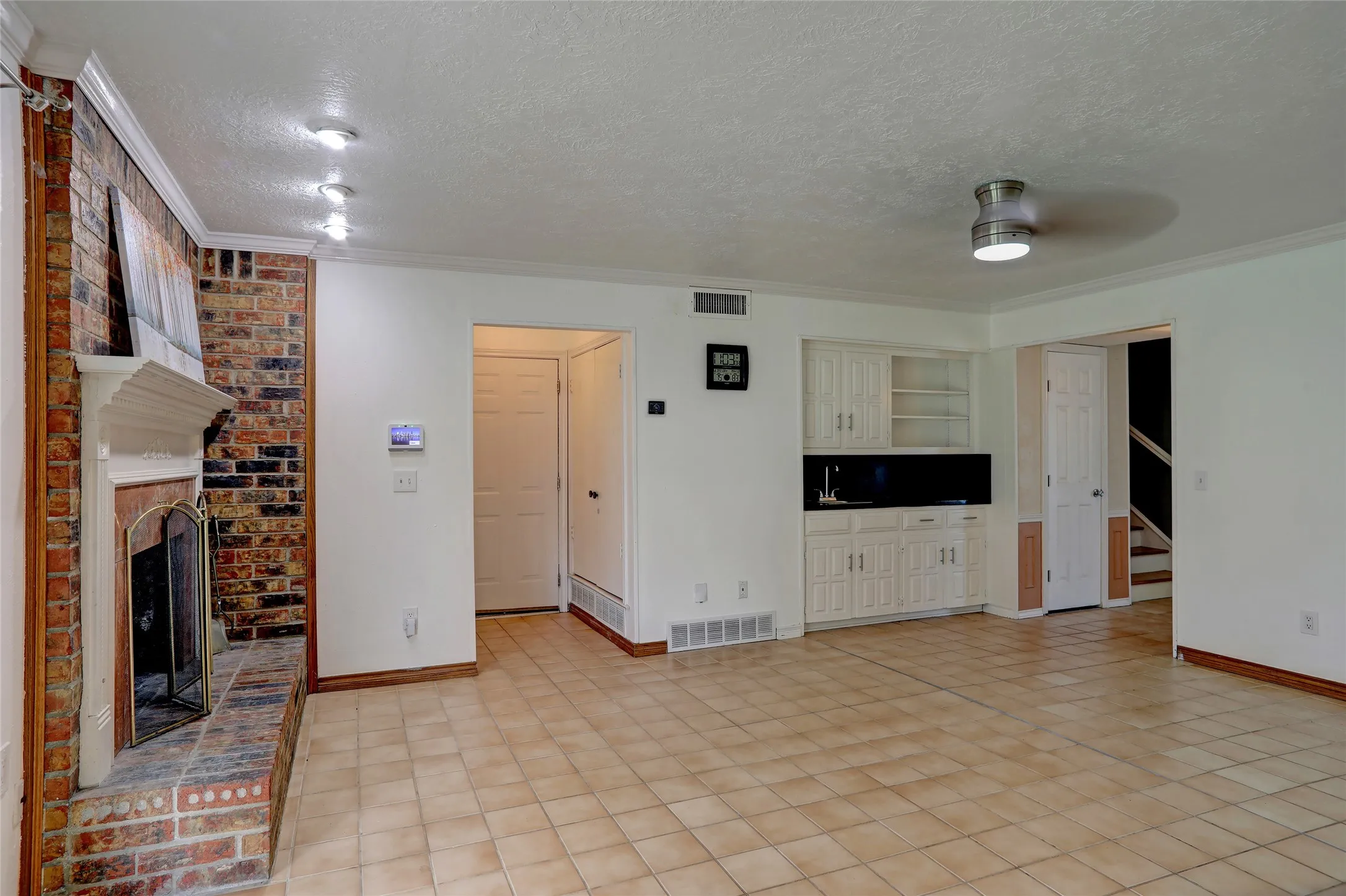 Spacious living area featuring a brick fireplace with a white mantel, tile flooring, and a built-in wet bar with white cabinetry